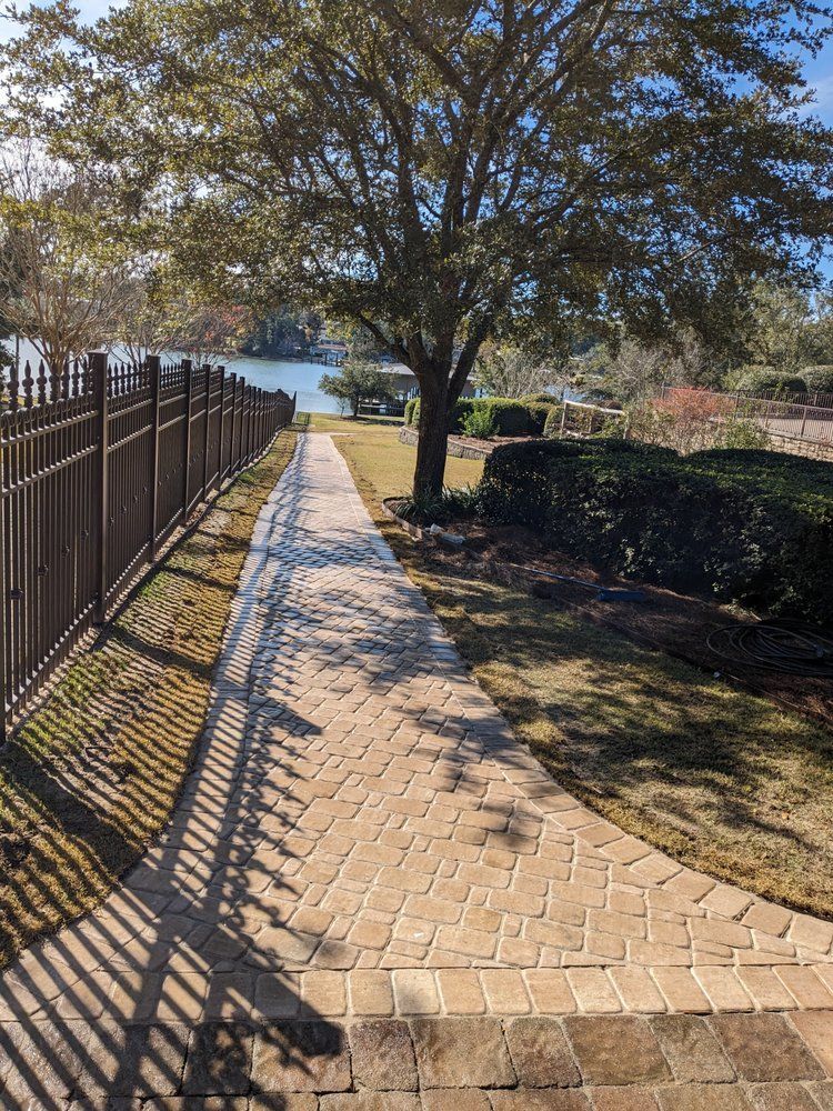 Brick path beside fence and tree leading to a lake on a sunny day