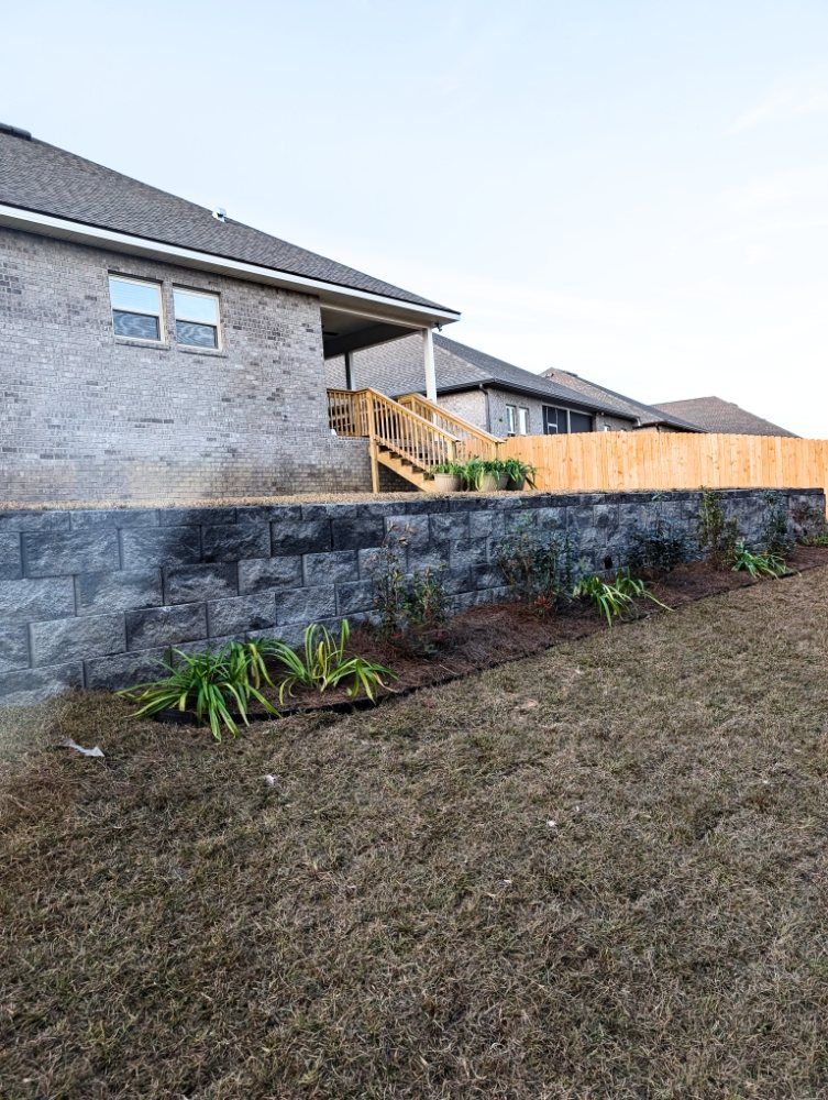 Backyard with stone retaining wall, wooden stairs, and a fenced lawn beside a house