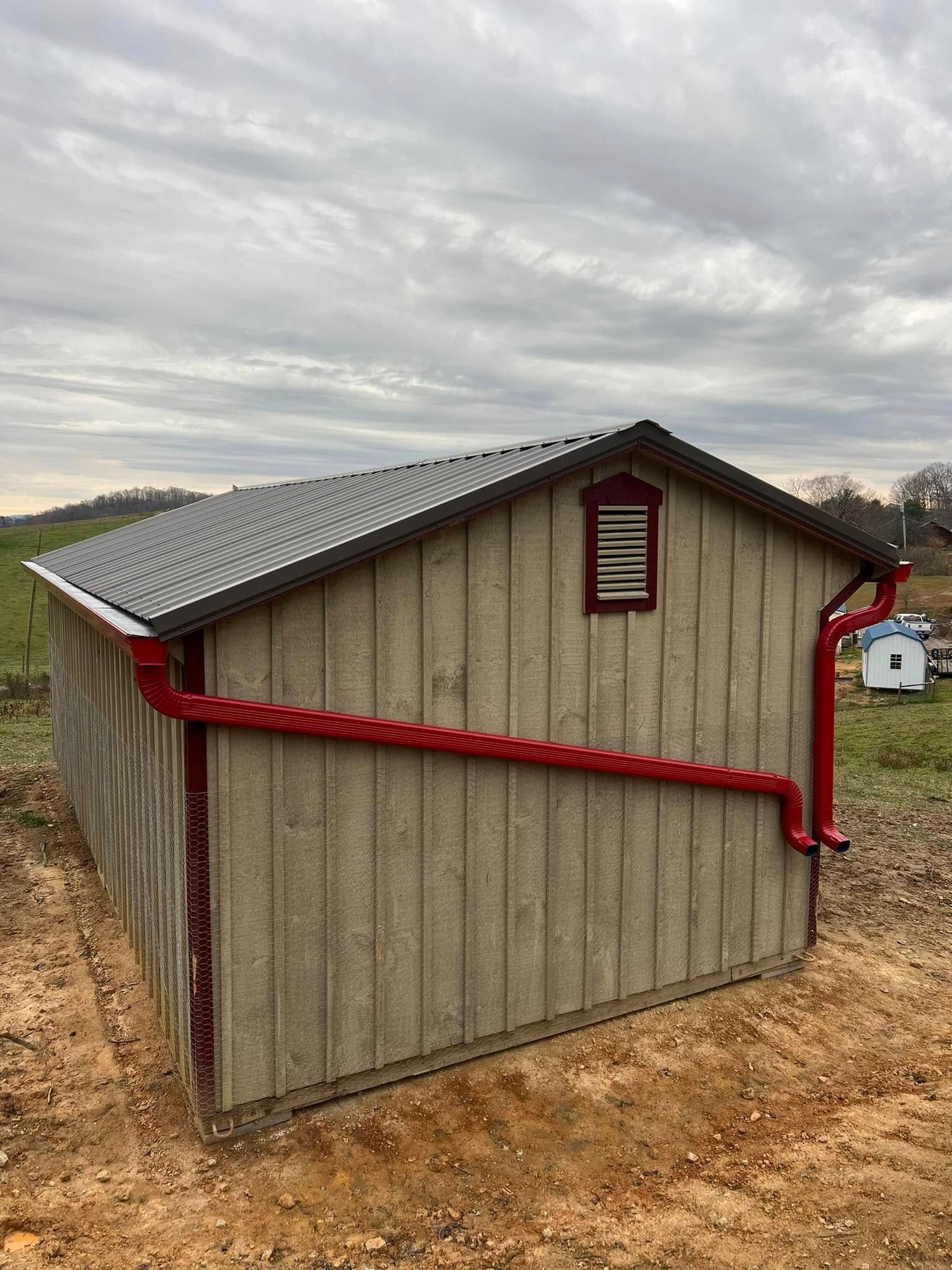 A tan shed with a dark roof and a red decorative gutter system installed diagonally across the side wall.