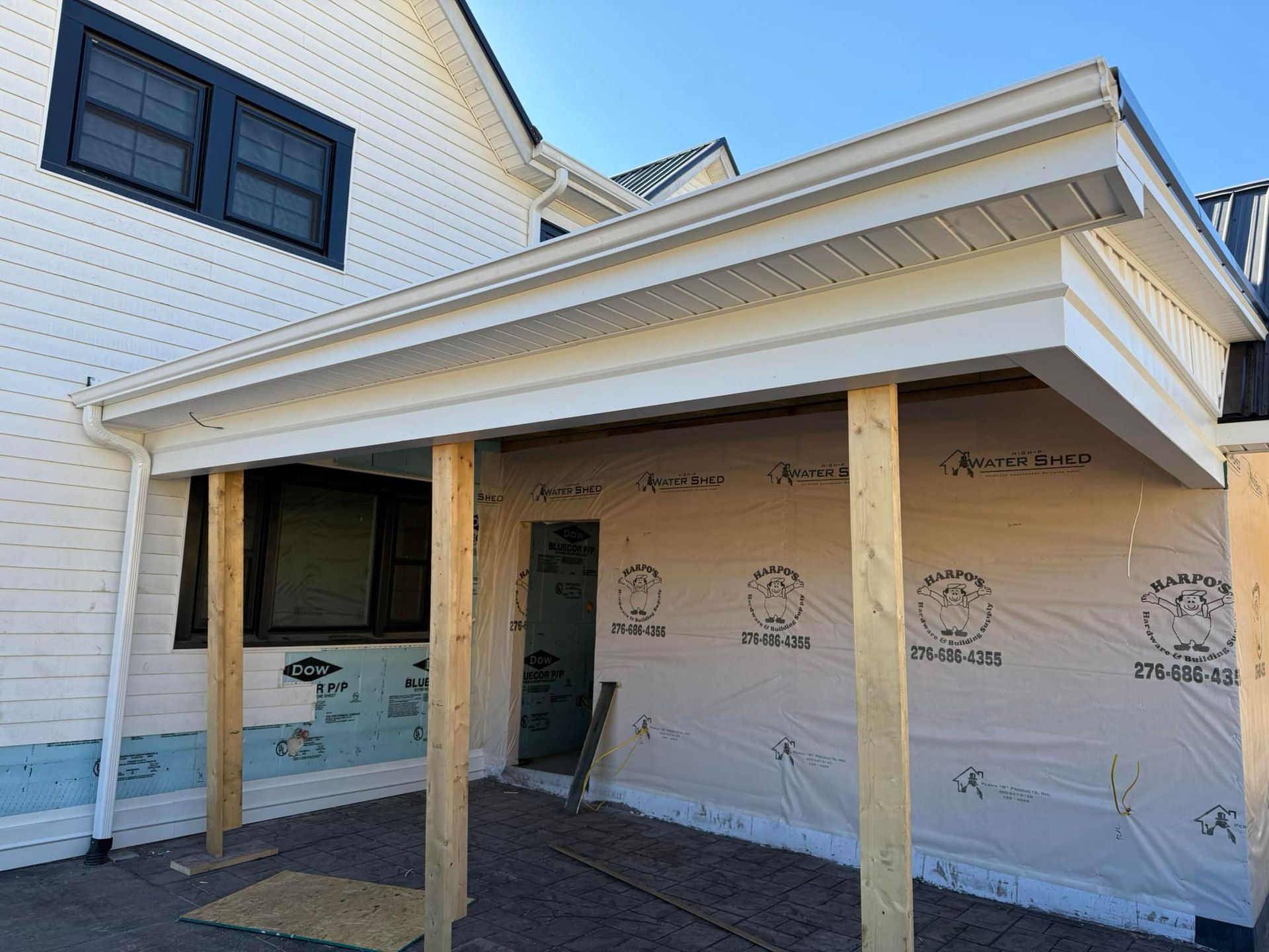 A white house exterior featuring a newly constructed porch frame with raw wooden posts and exposed protective house wrap.