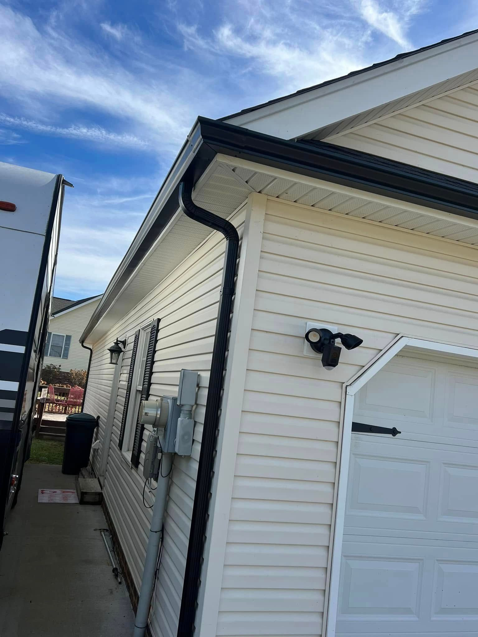A low-angle view of a beige house exterior with black gutters, a white garage door, and a parked RV on the left.