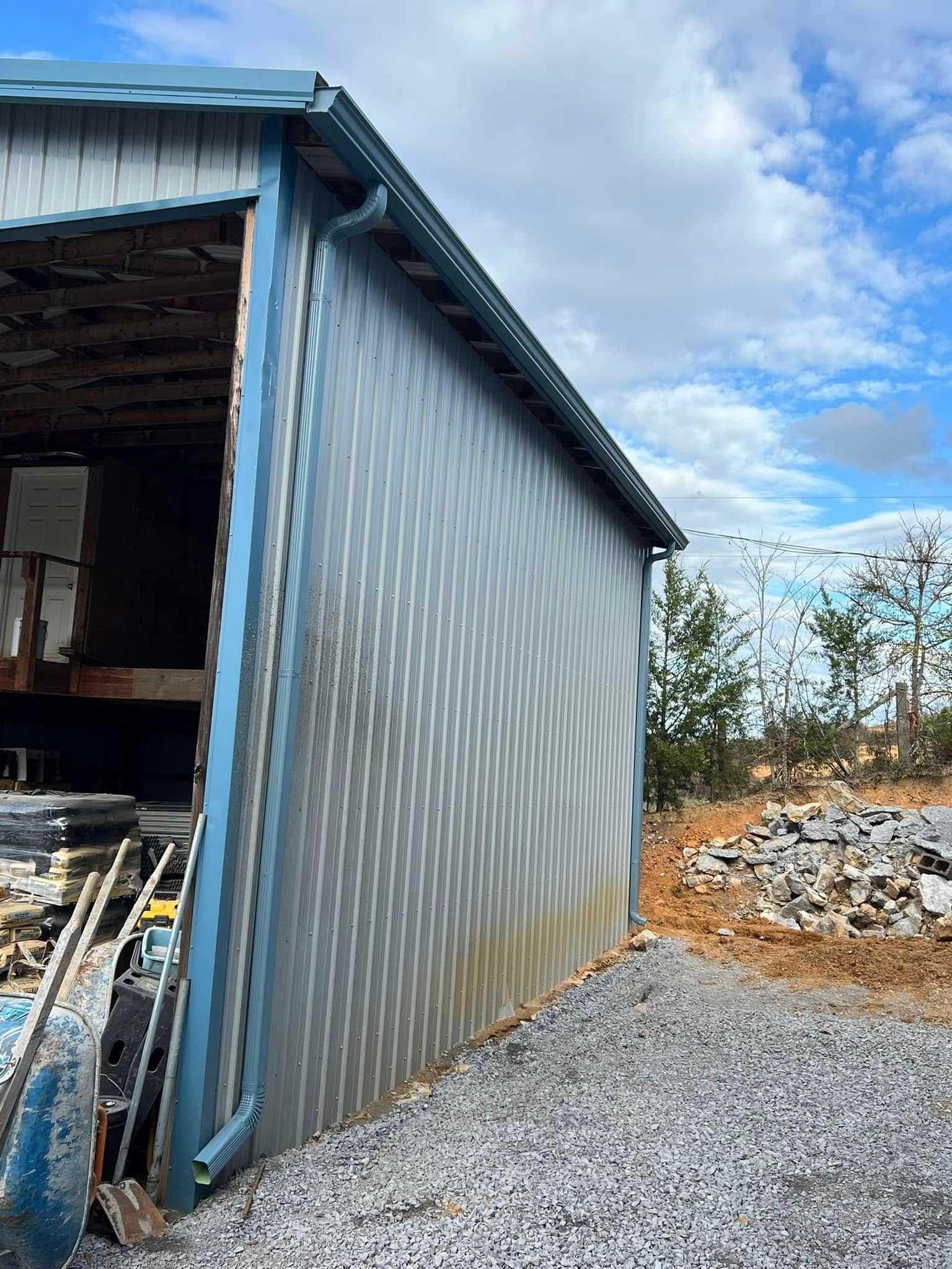 A blue-framed metal shed structure sits on a gravel lot under a blue sky with scattered clouds.
