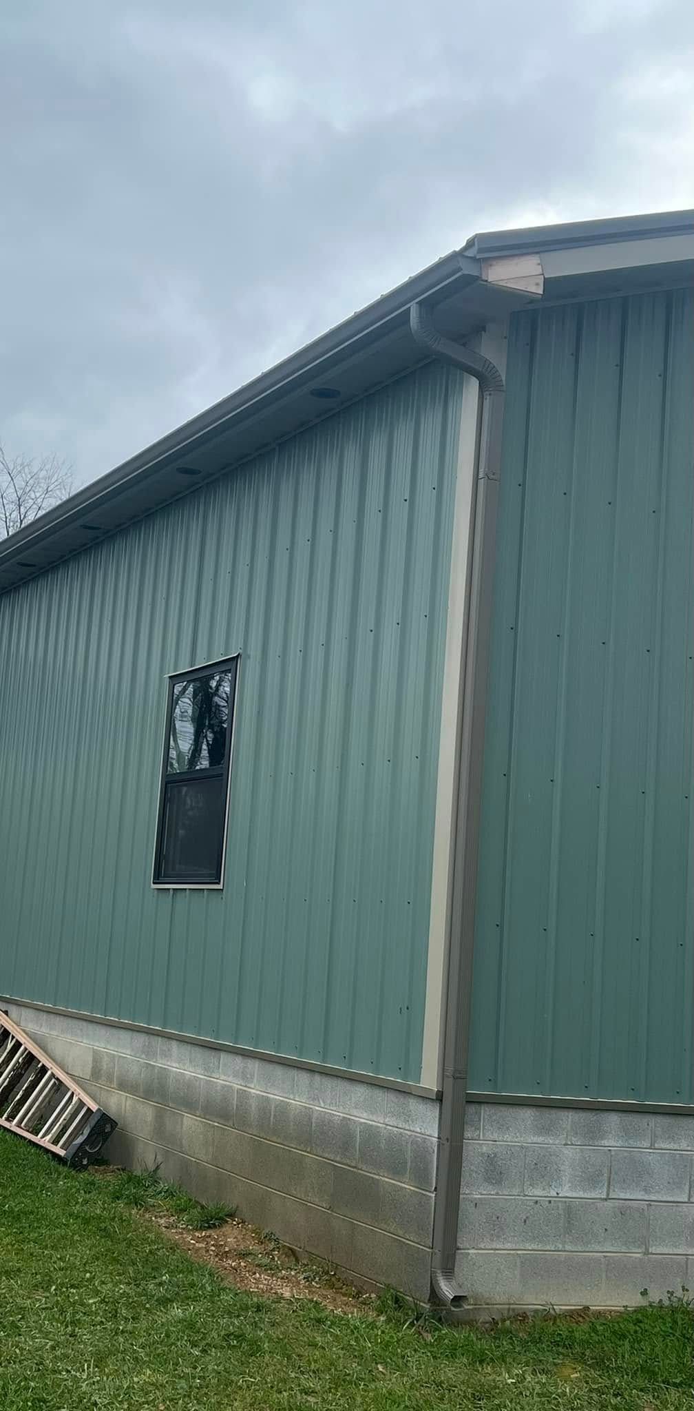 Exterior view of a light green metal-sided building with a single window, a concrete foundation, and a drainpipe.