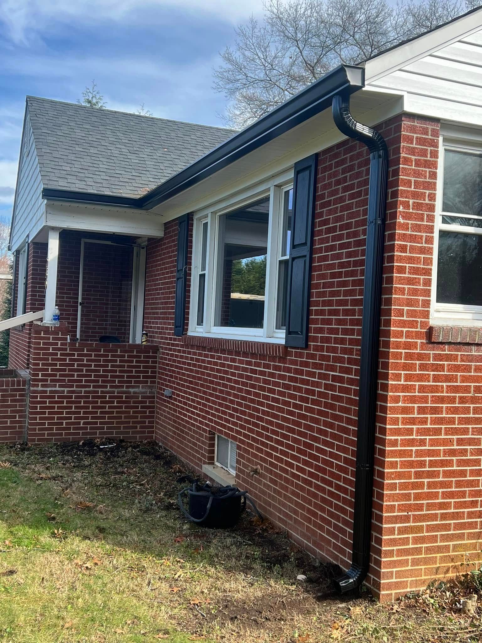 Exterior of a red brick house featuring a dark gutter and downspout, white window frames, and blue shutters.