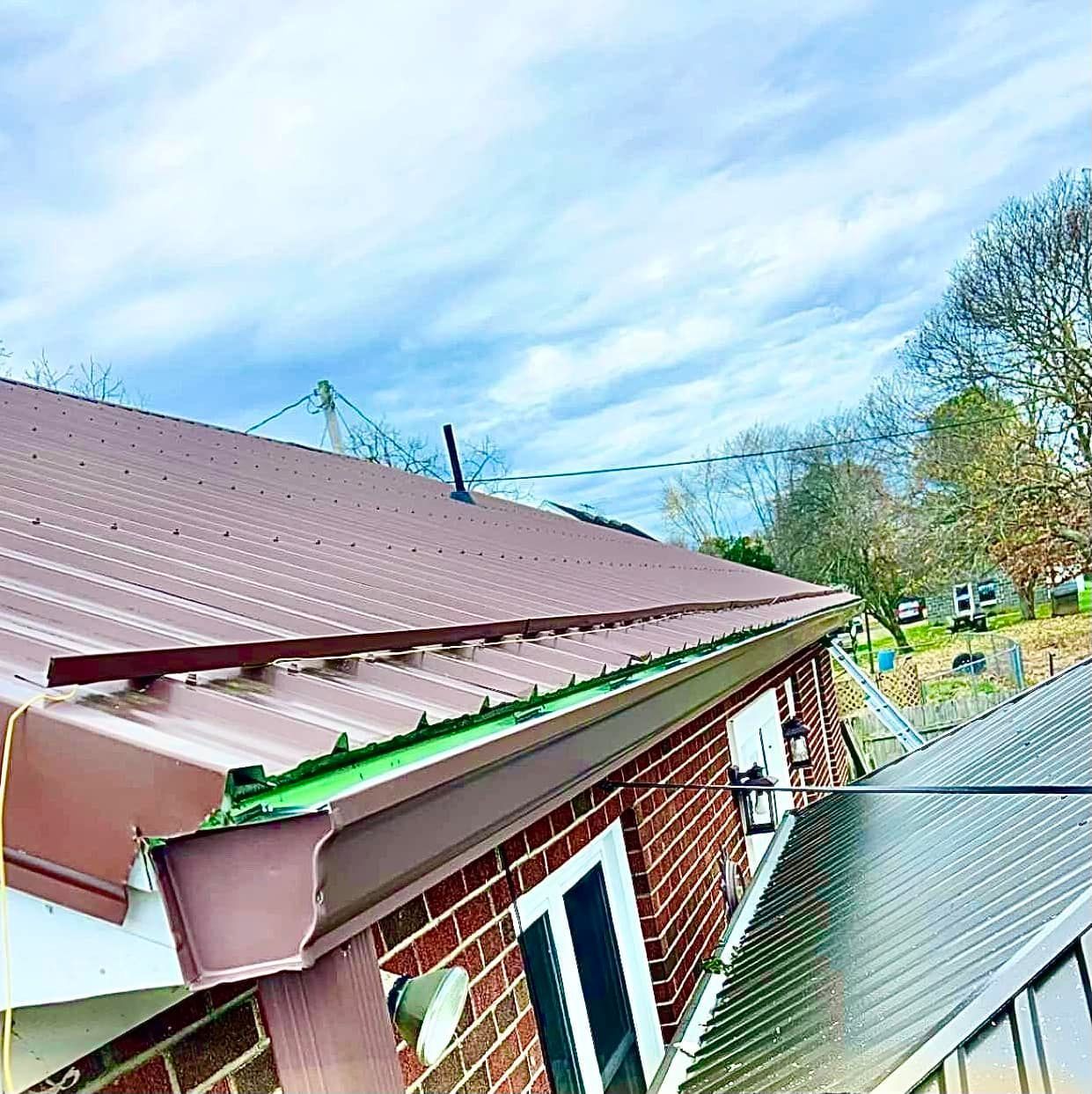 A brown metal roof with a gutter running along the edge, viewed from an elevated angle above a brick building.