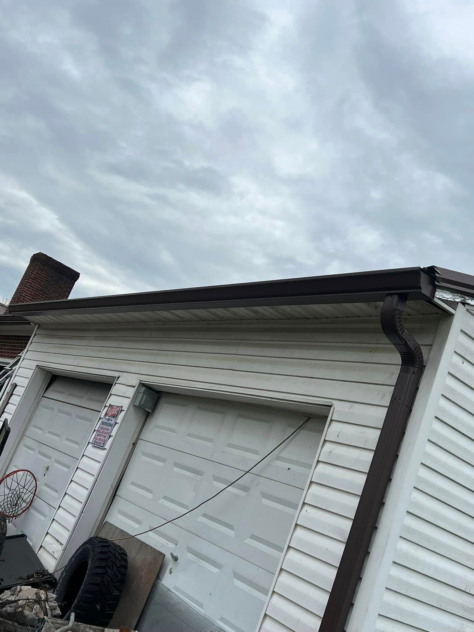 A white detached garage with dark brown gutters and trim under a cloudy sky.