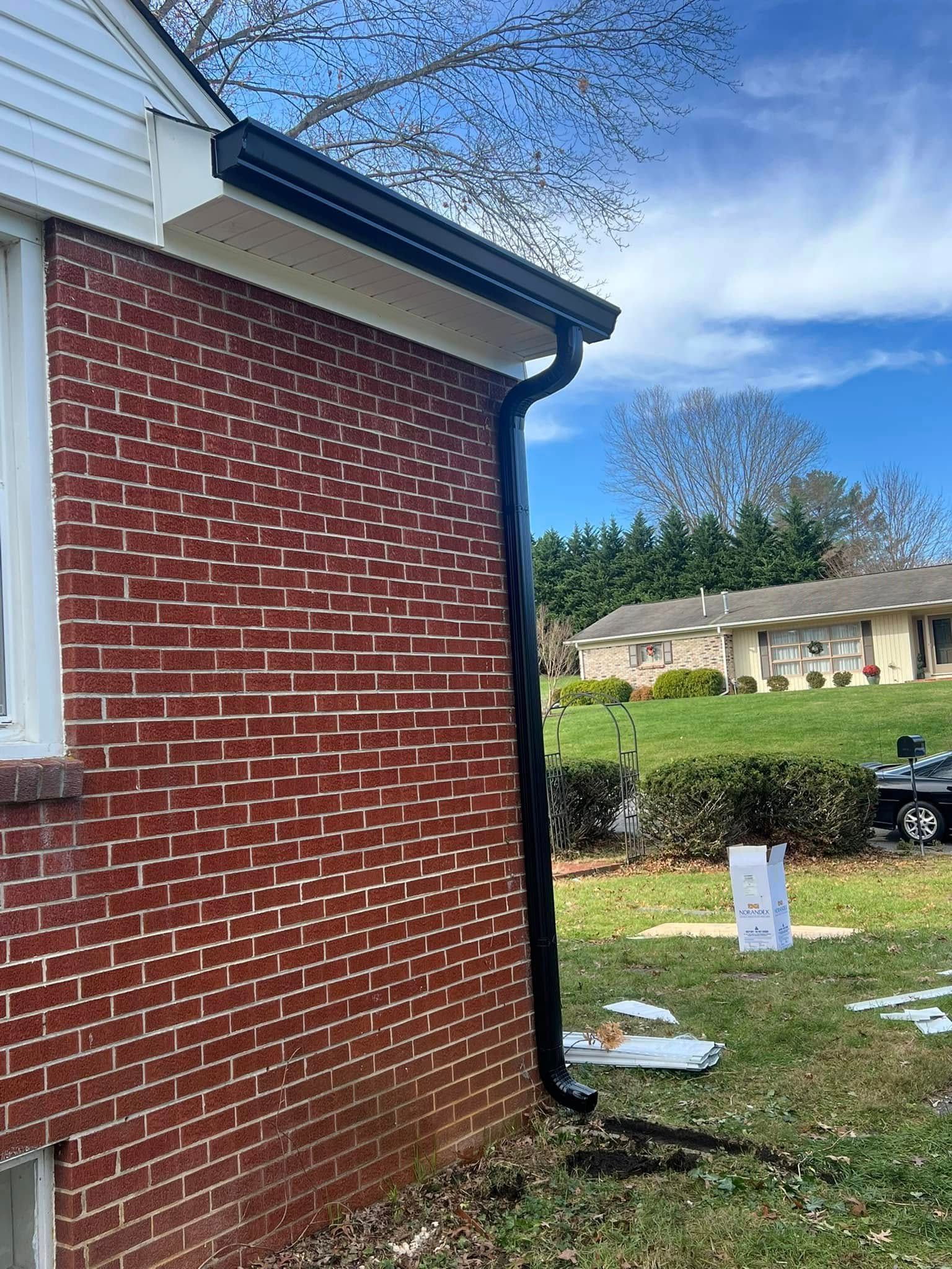 Black gutter and downspout installed on the corner of a red brick house with a white roof edge.