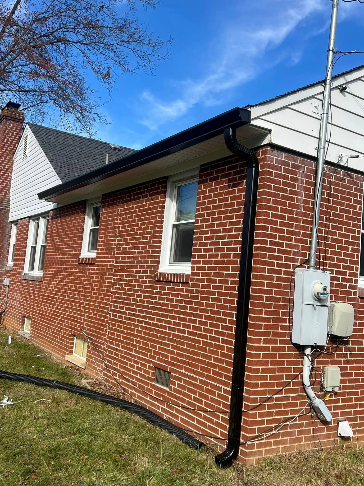 Exterior corner of a red brick house with white trim, a black gutter, and electrical equipment mounted on the wall.