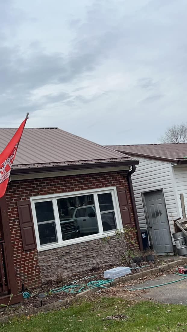 A red brick house with a brown metal roof, a white-framed window, and a red flag attached to the porch.