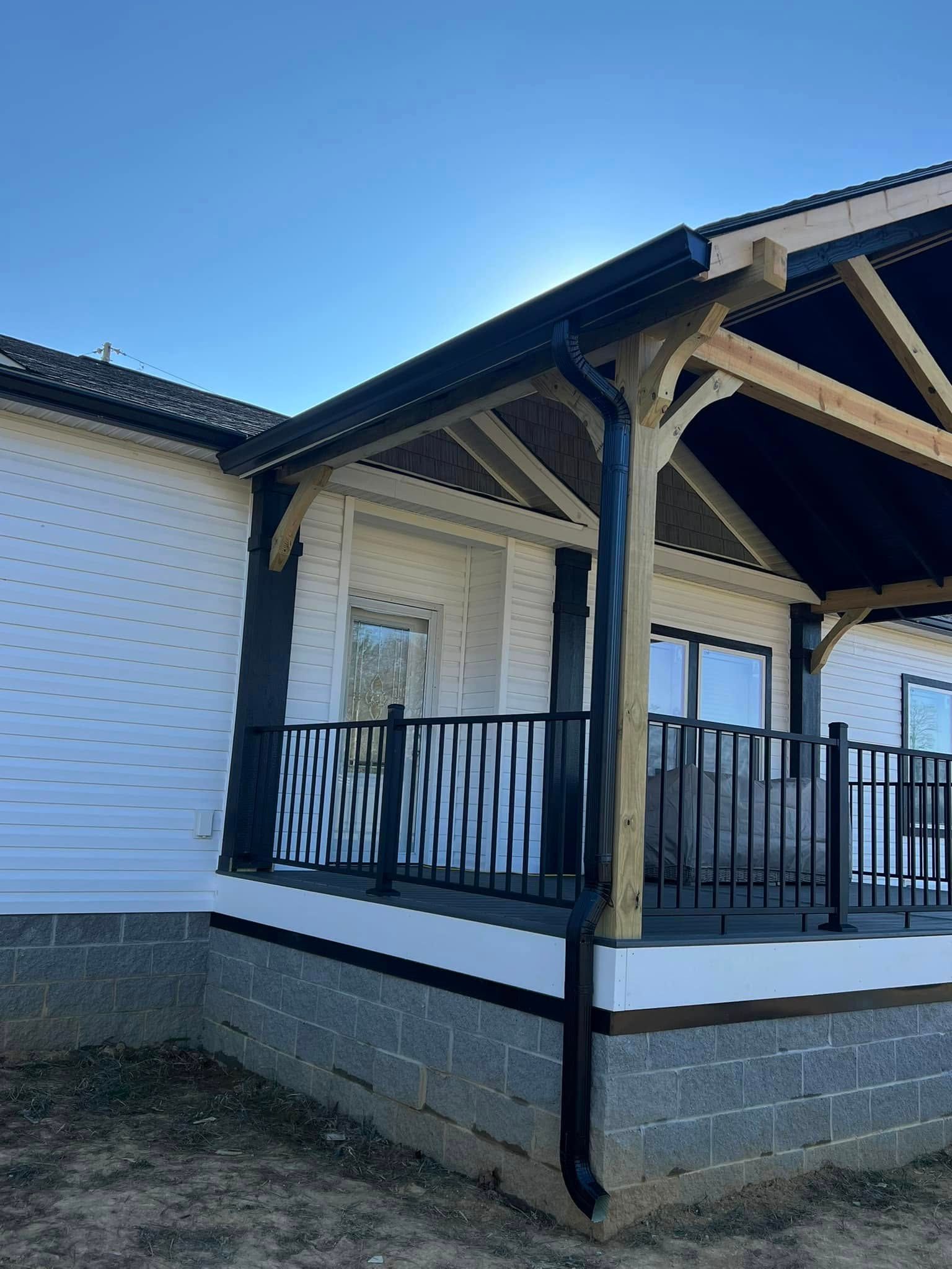 A house exterior with a white siding, a covered wooden porch, black metal railings, and a concrete block foundation.