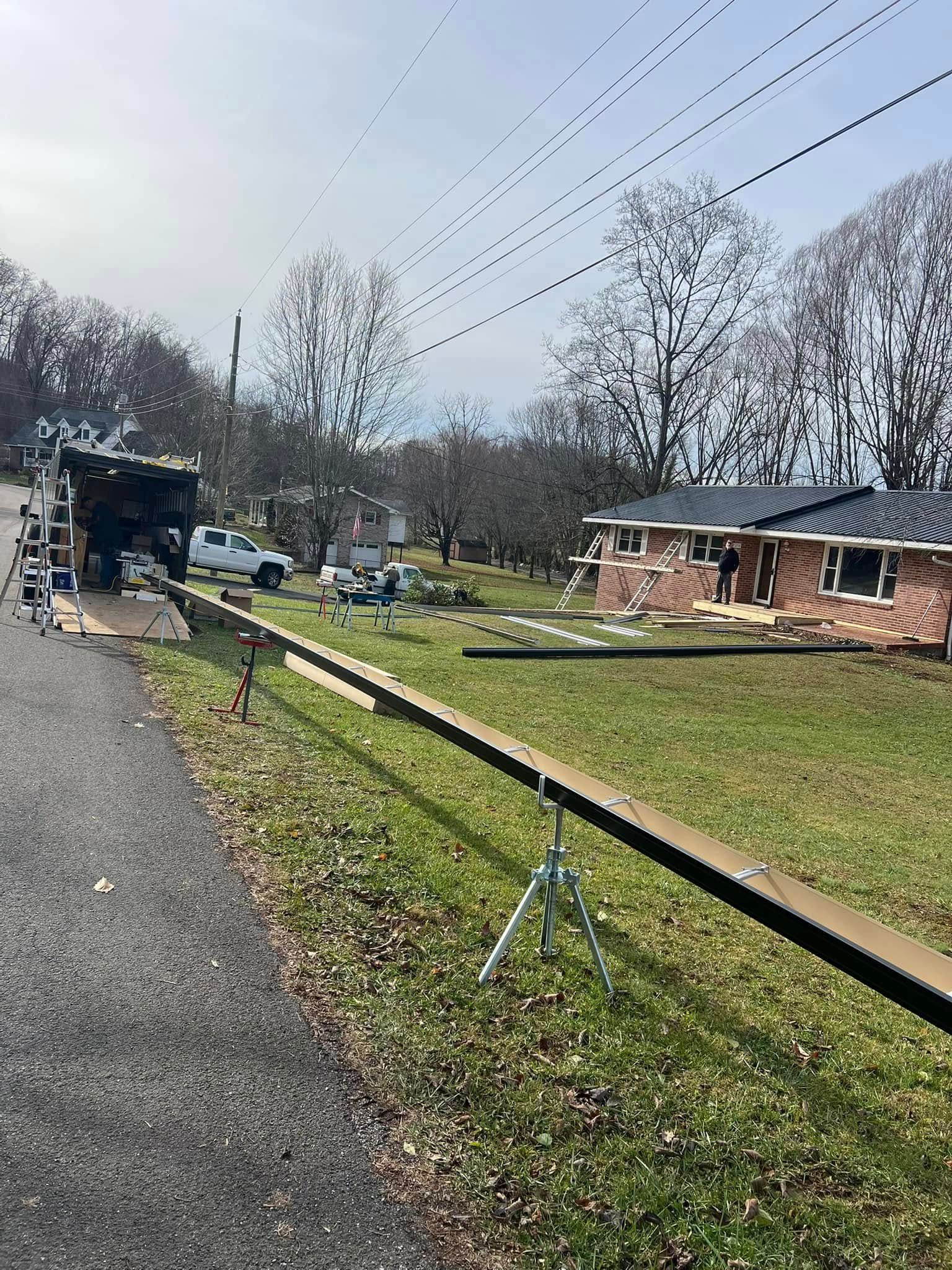 Workers install a long support beam near a house, with a truck and equipment visible on a grassy, suburban lot.