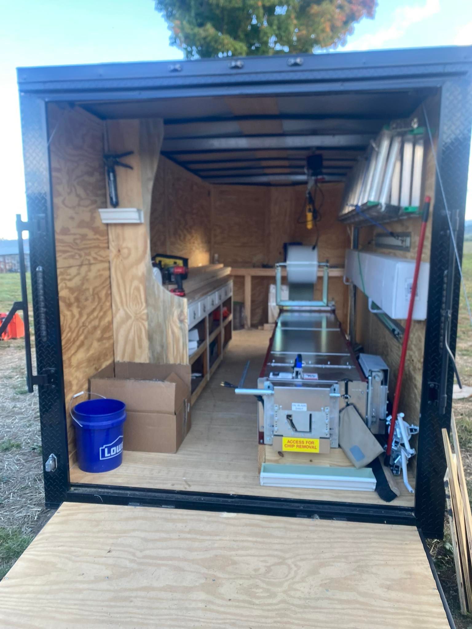 Inside of a cargo trailer equipped with shelving, tools, a blue bucket, and a metal bending brake for construction work.