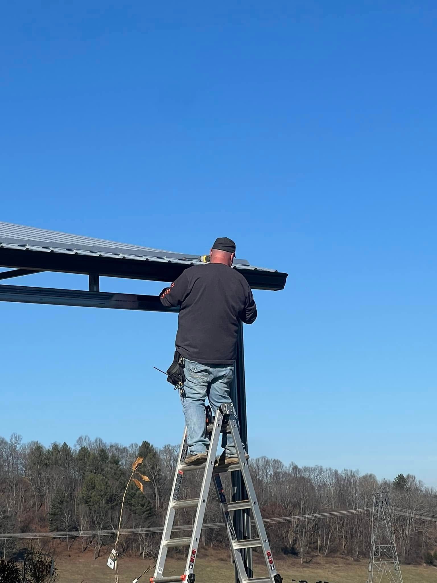 A person stands on a ladder, working on the metal frame of an outdoor structure under a clear blue sky.