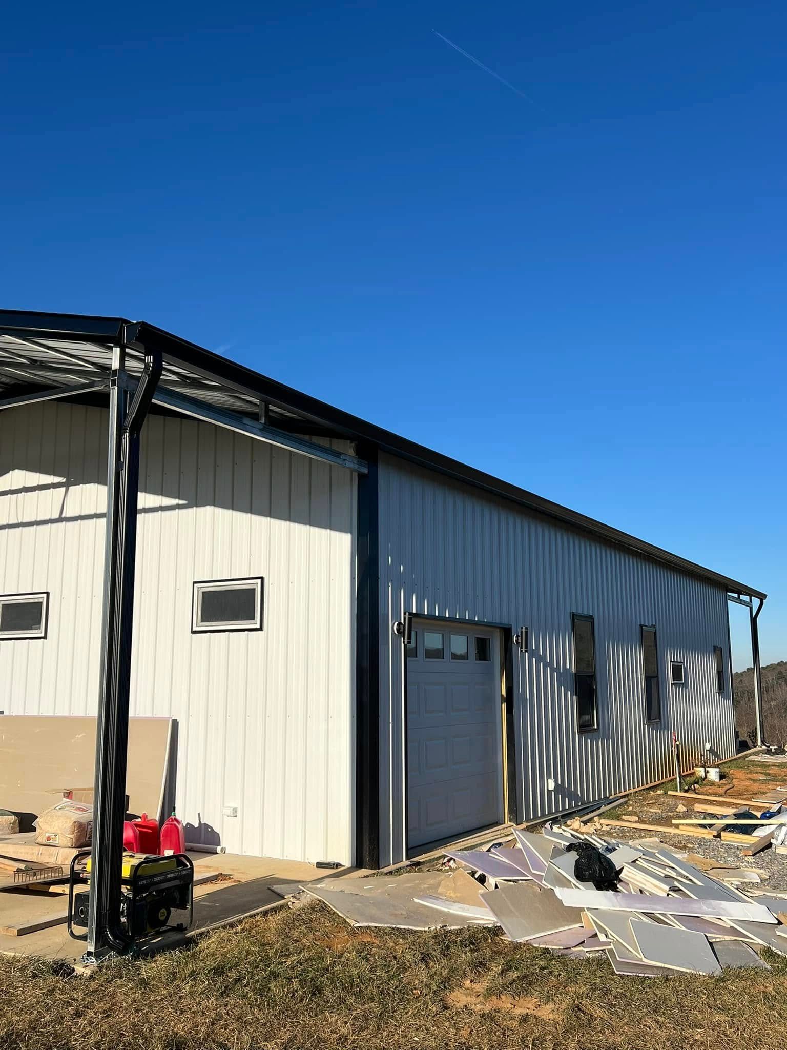 A single-story metal building with a white exterior, black trim, and garage door stands under a clear blue sky.