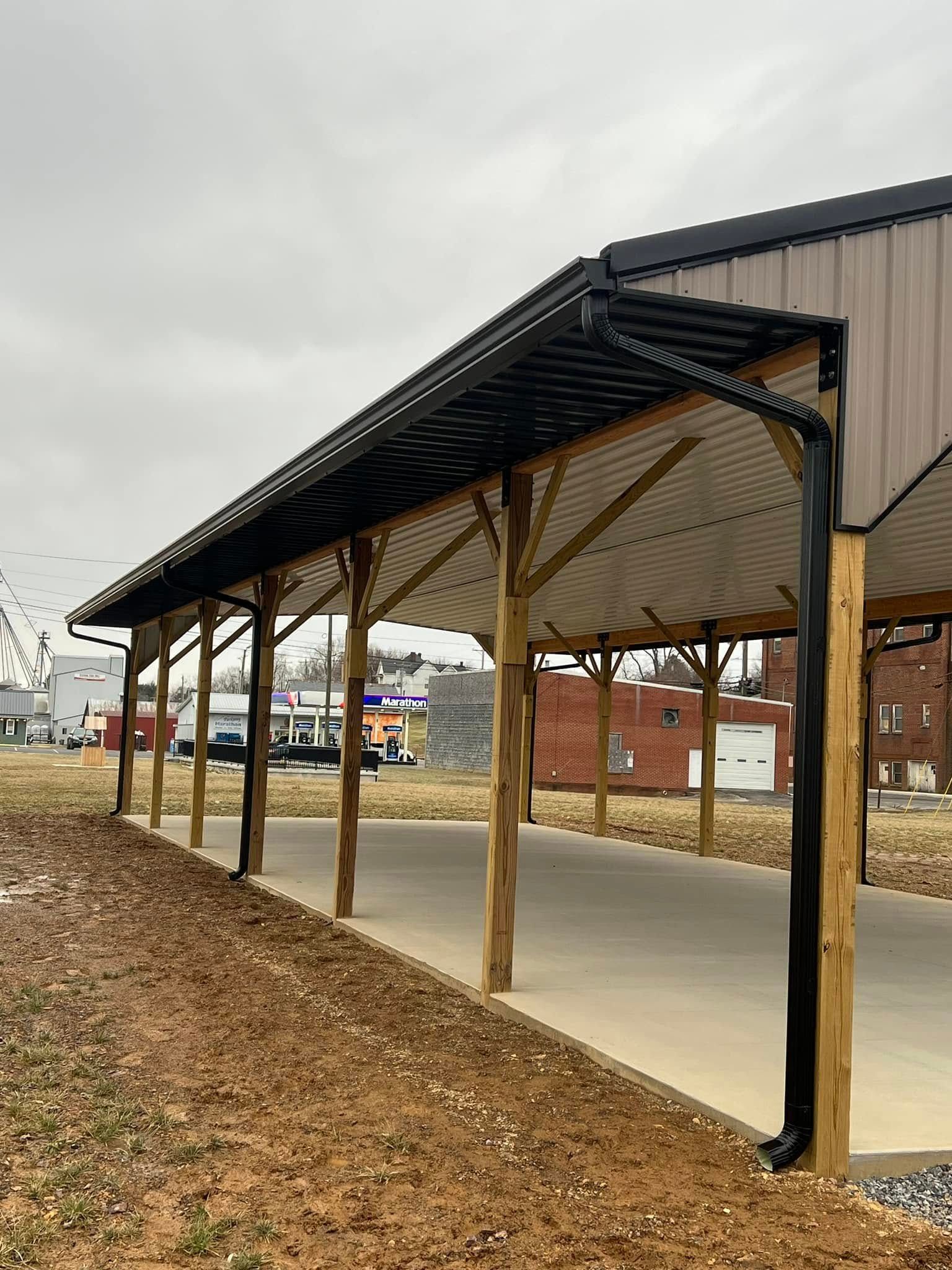 A covered outdoor pavilion with a concrete slab, wooden support posts, and black metal roofing and gutters.