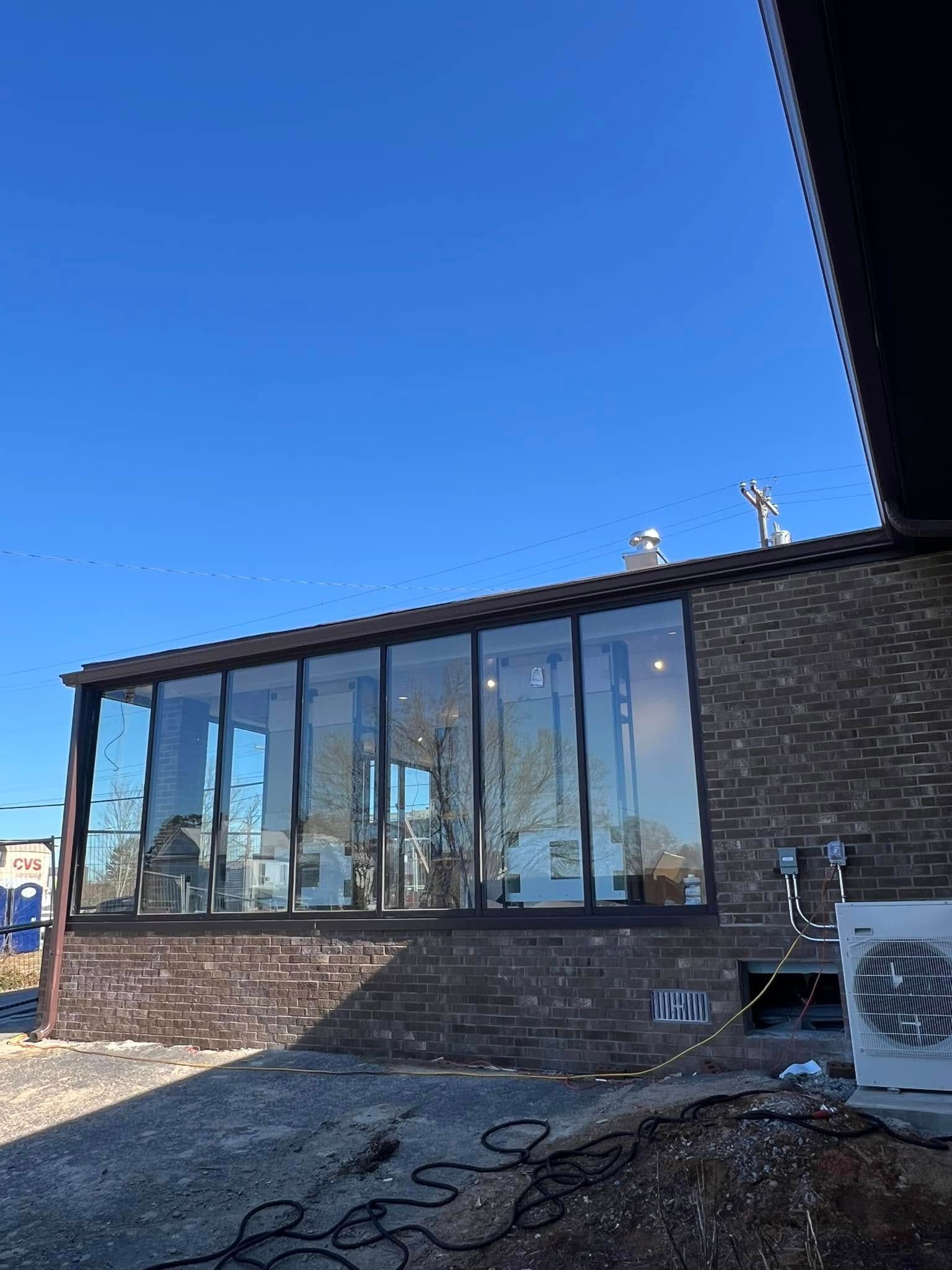 A modern brick building featuring a large, floor-to-ceiling glass wall under a clear blue sky.