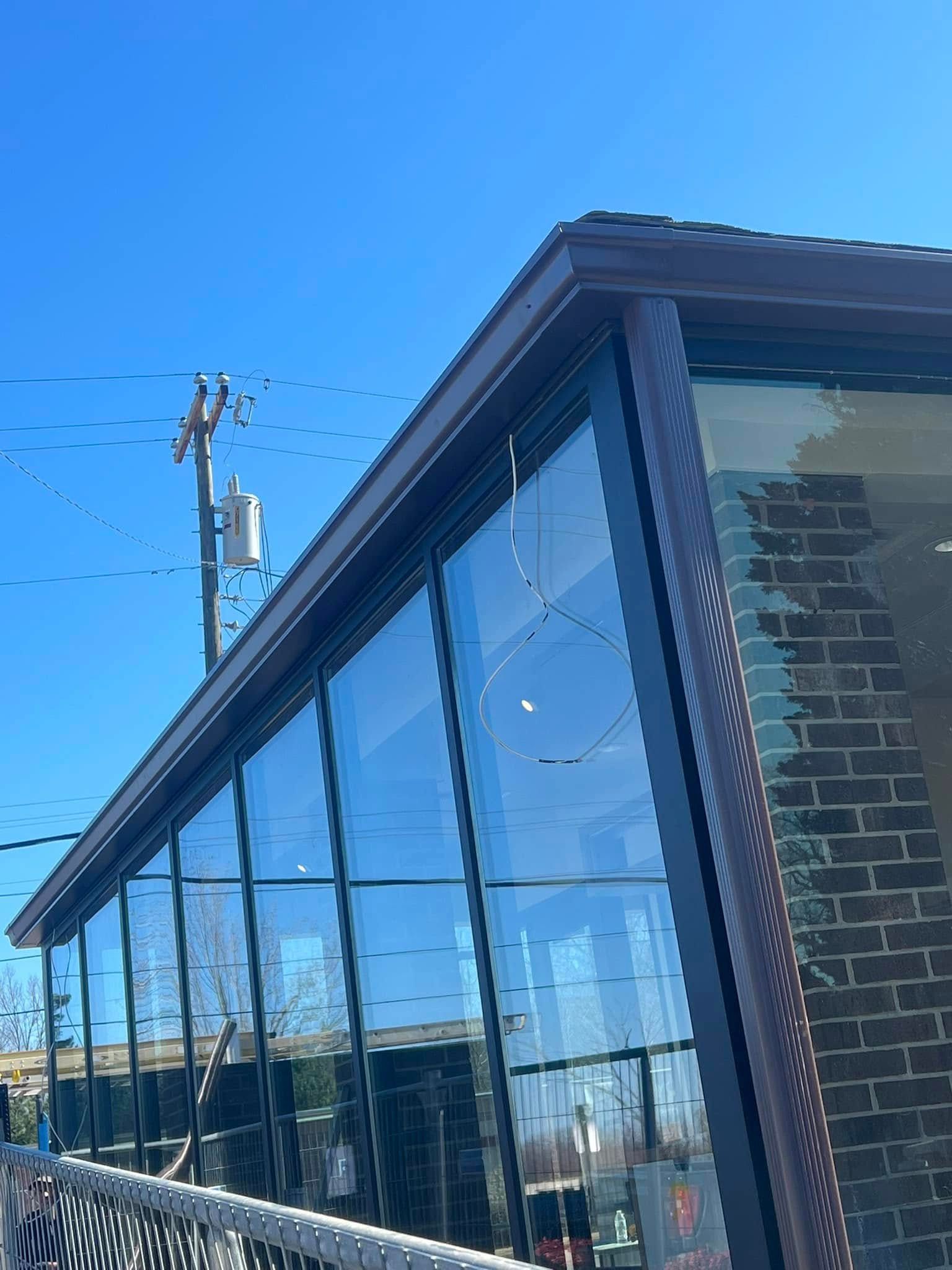 A low-angle view of a brick building with a glass-enclosed patio, under a clear blue sky with a utility pole nearby.