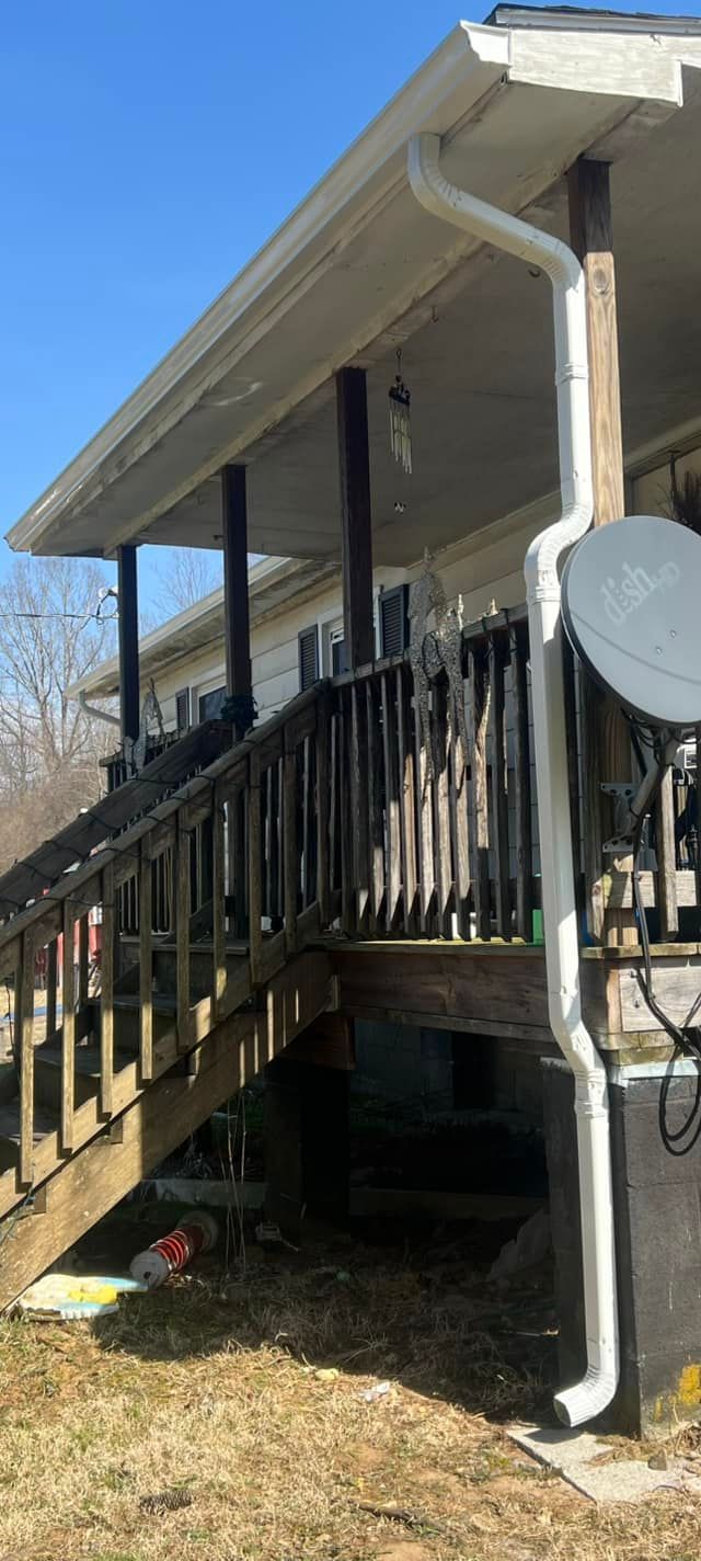 A white downspout attached to the corner of a wooden porch and house exterior on a sunny day.