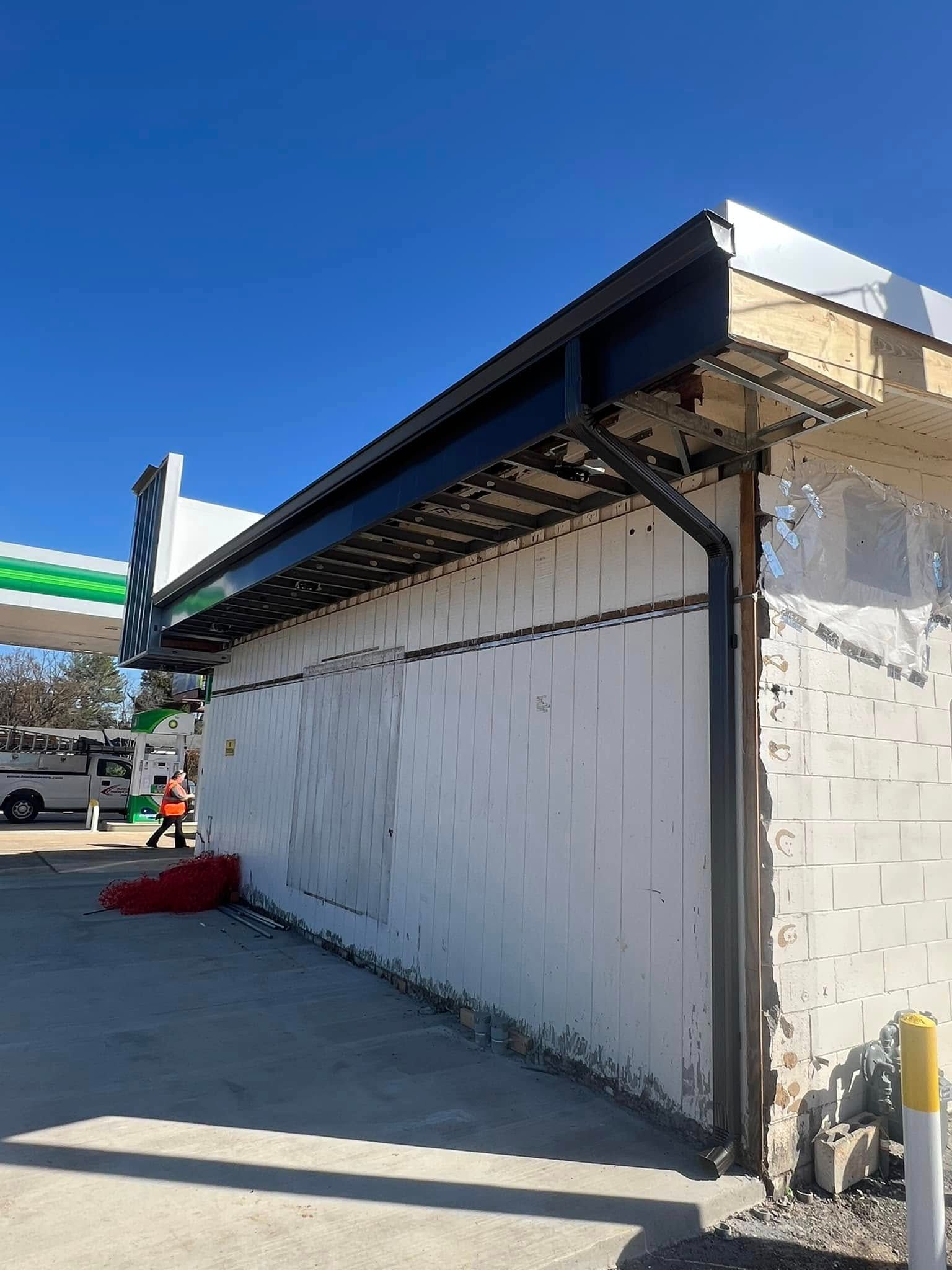 A exterior side view of a white cinder block building under renovation with a newly installed black roof trim and gutter.