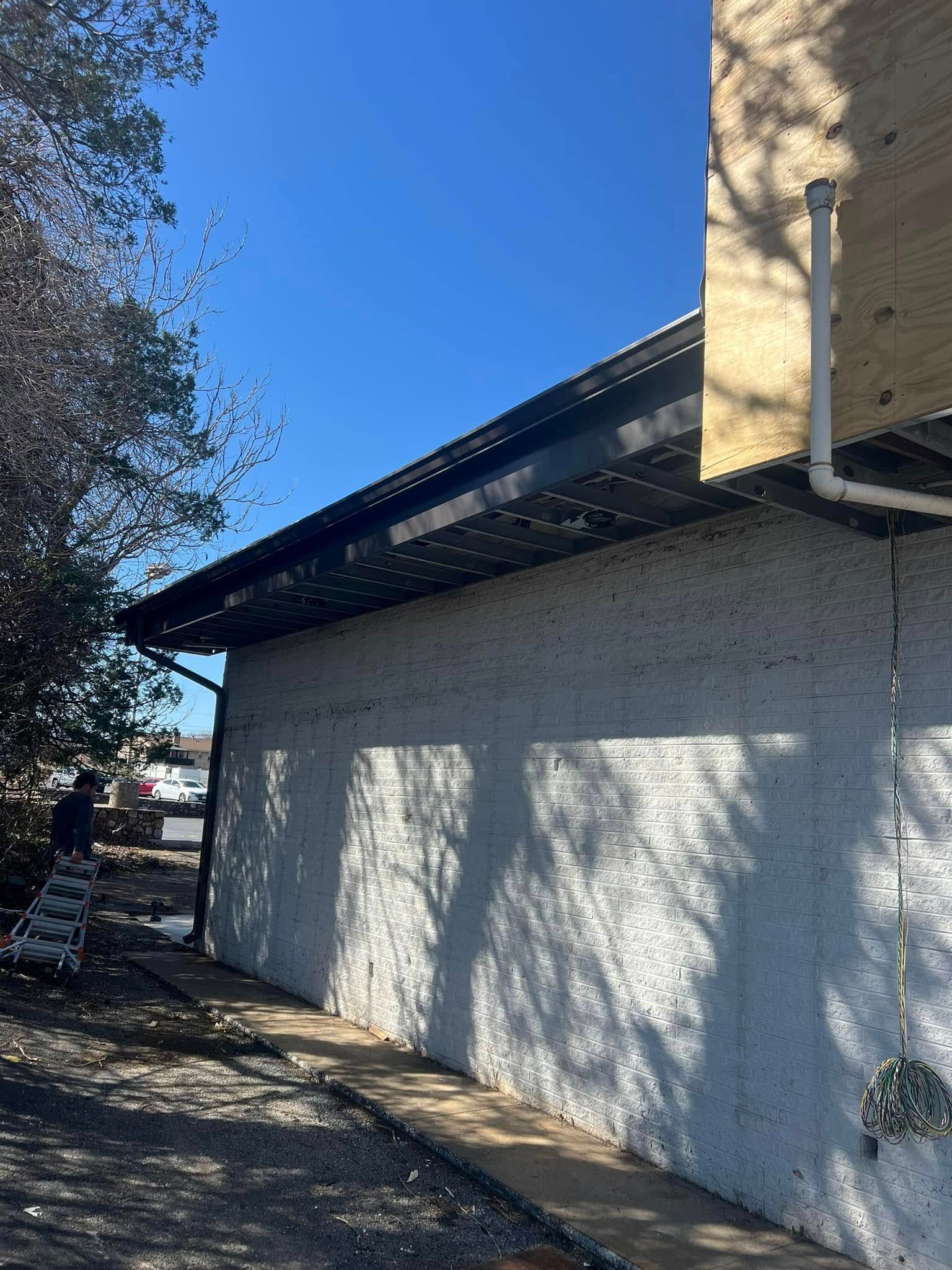 A white stucco building wall with a dark roofline and a vertical drainage pipe under a clear blue sky.