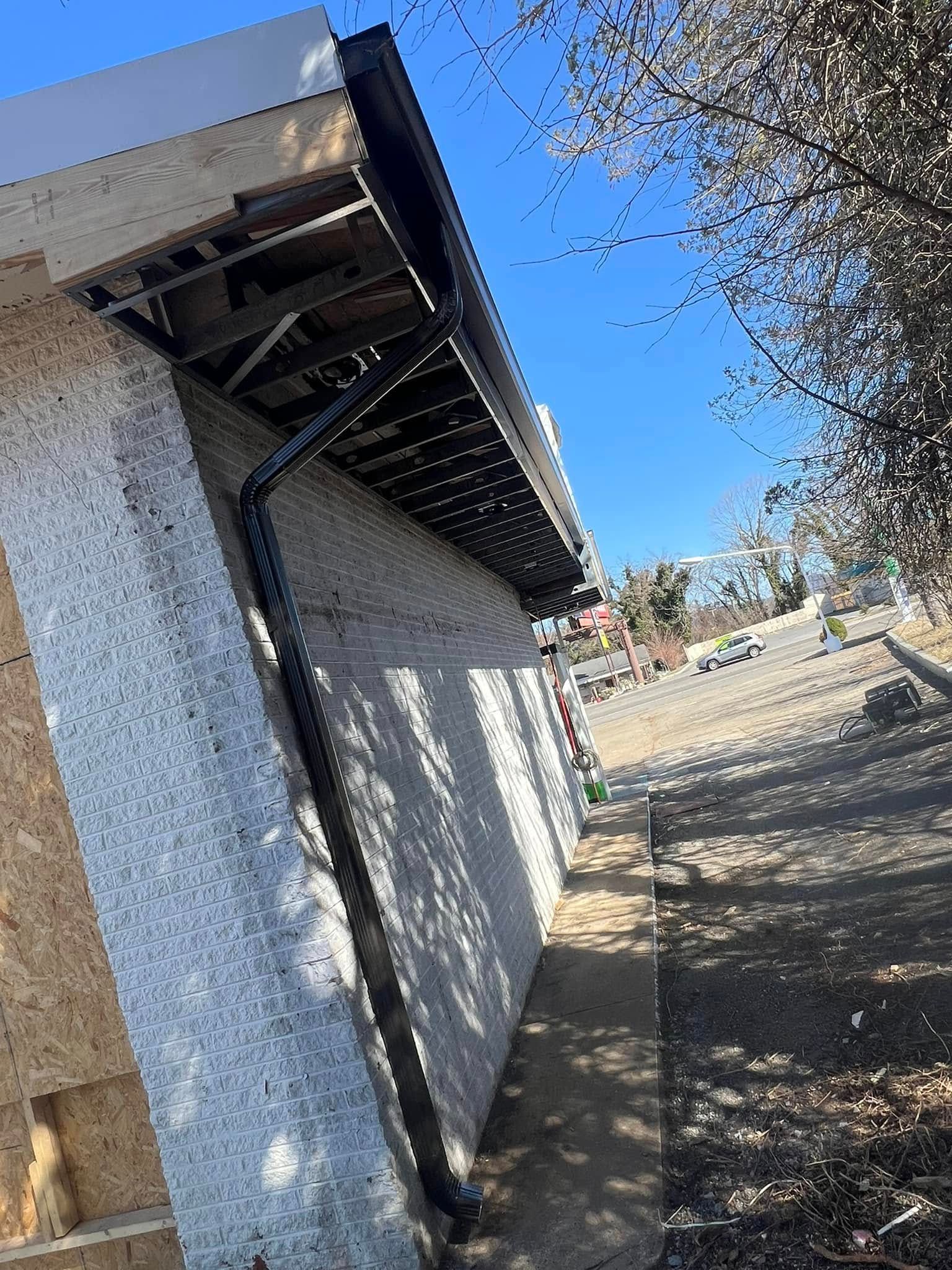 An exterior view of a building under construction, showing a black downspout attached to a light-colored stucco wall.