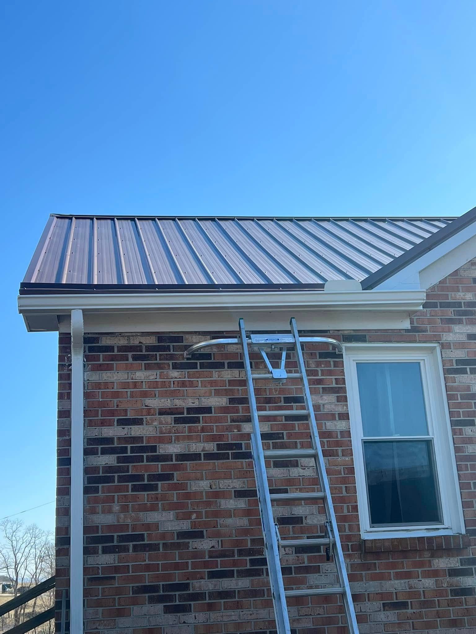 A metal ladder leans against a brick house exterior, reaching up toward the roofline and rain gutter.