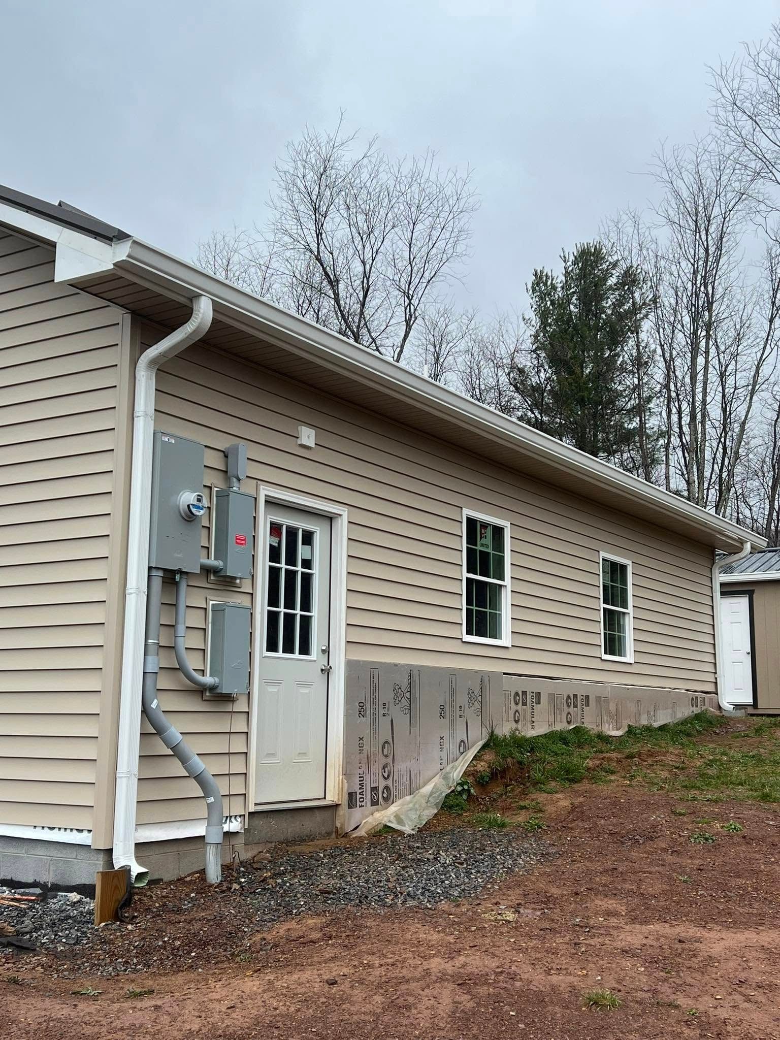 Light tan horizontal vinyl siding on the exterior of a home with a white door, two windows, and an electrical box setup.