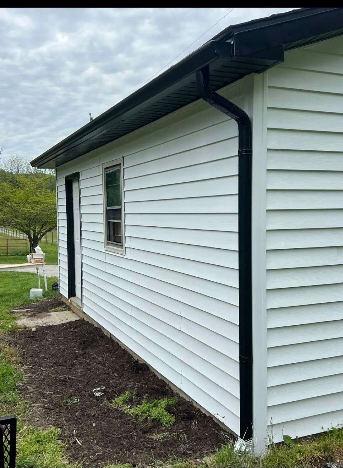 Side view of a white, horizontal-sided building with a black roof edge, black rain gutters, and a black window frame.
