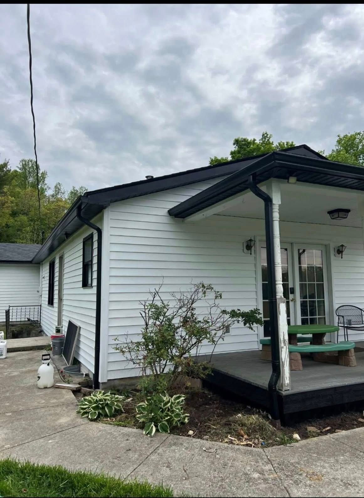 A white house with black trim and roof, featuring a small covered porch, a green bench, and a concrete walkway.