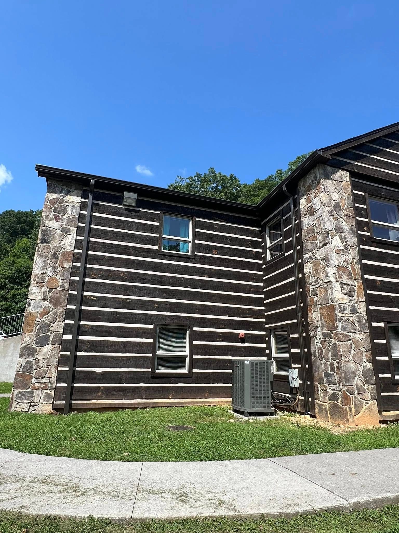 A two-story log building with stone corners, horizontal dark logs, white chinking, and an outdoor air conditioning unit.