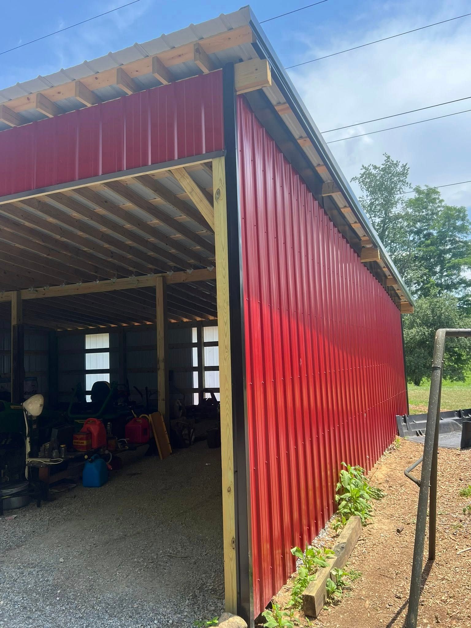 A bright red, corrugated metal wall installed on the corner of a wooden, open-sided structure outdoors.
