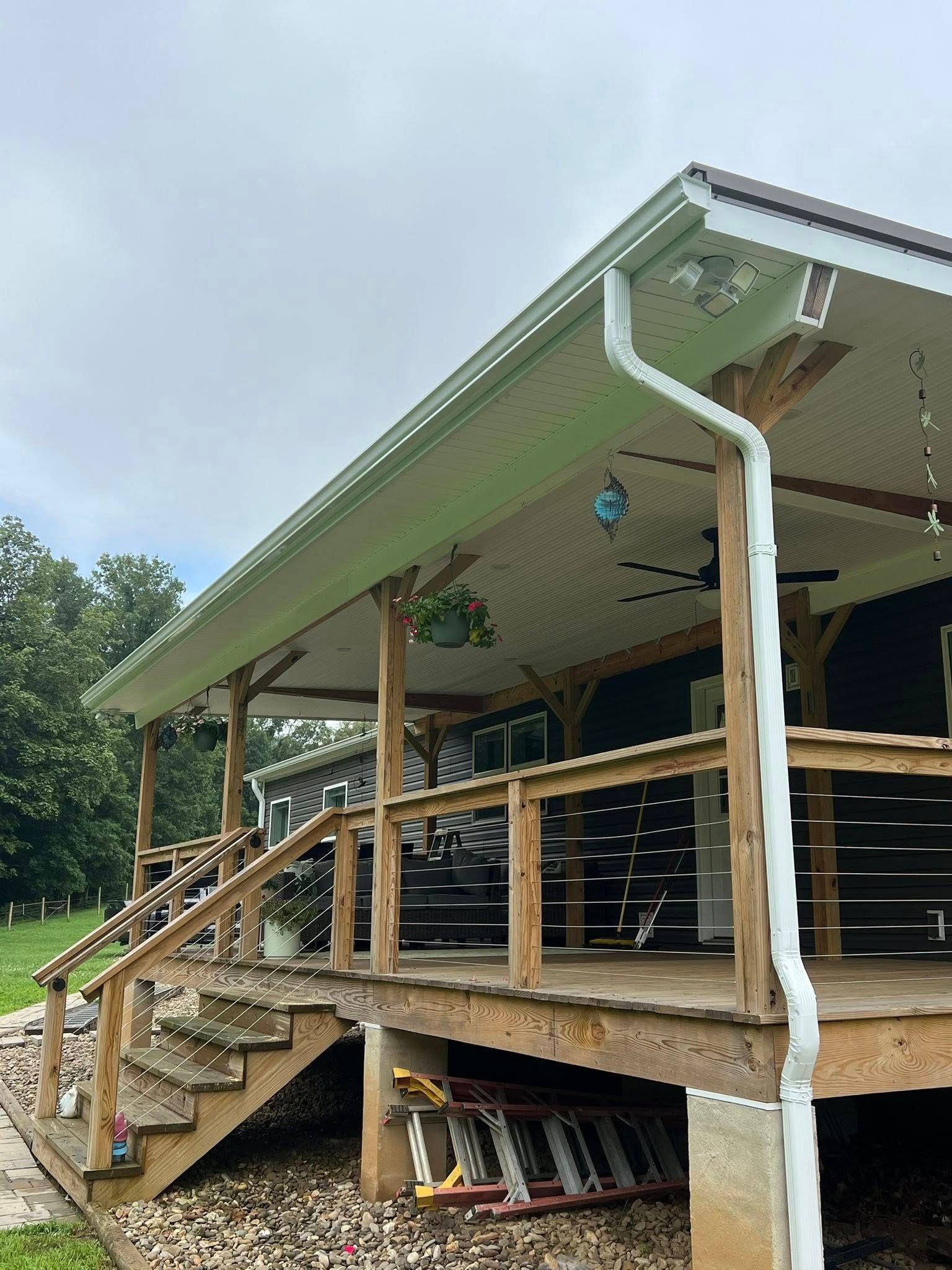 A wooden deck and porch with a railing and stairs on the side of a house, featuring a white gutter and outdoor lights.
