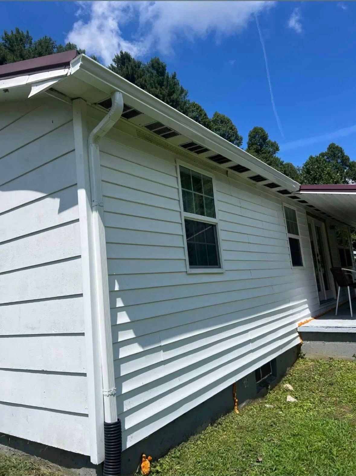 A white house exterior featuring lap siding, a roof with white gutters and a downspout, against a blue, sunny sky.