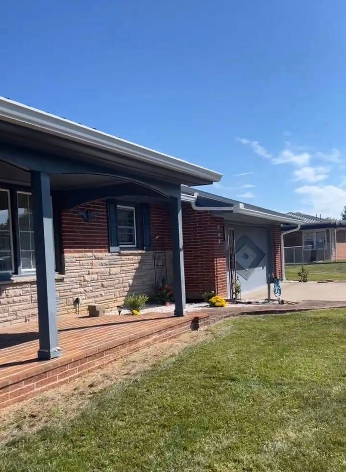 A single-story brick house with a stone front, covered porch, and attached garage under a clear blue sky.