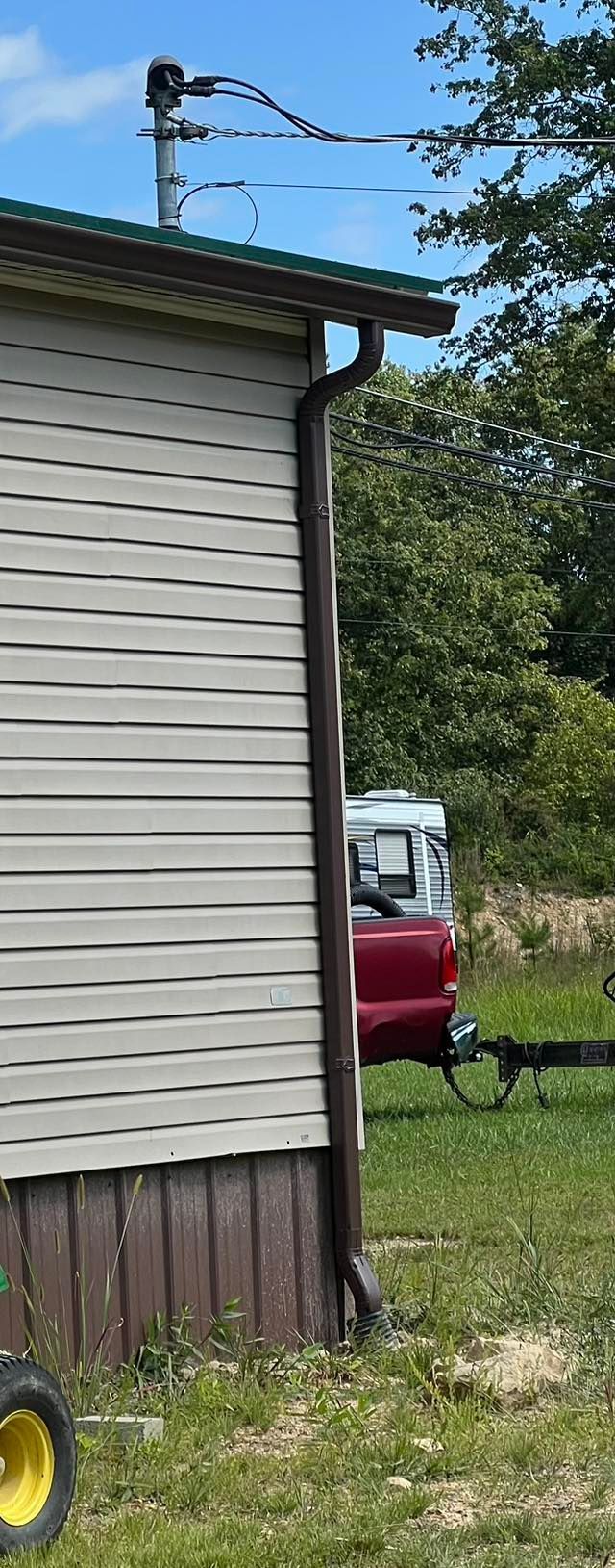 A side view of a house with beige siding and a downspout, featuring an electrical service mast on the roof.