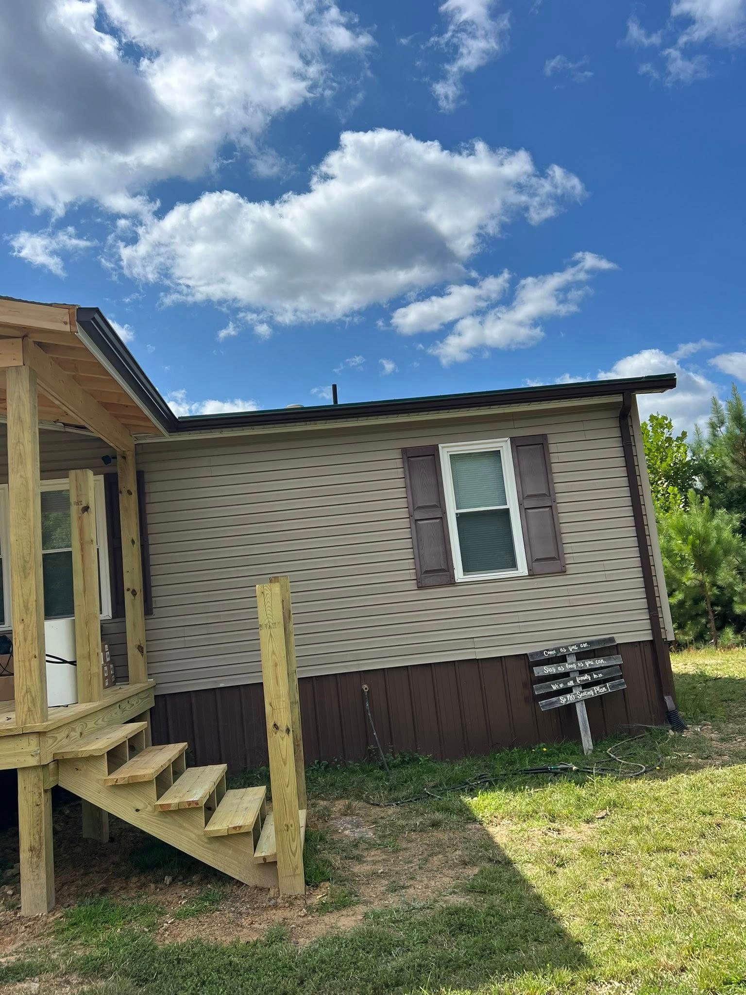 A tan manufactured home with brown trim and shutters, featuring a newly built wooden porch and steps against a blue sky.