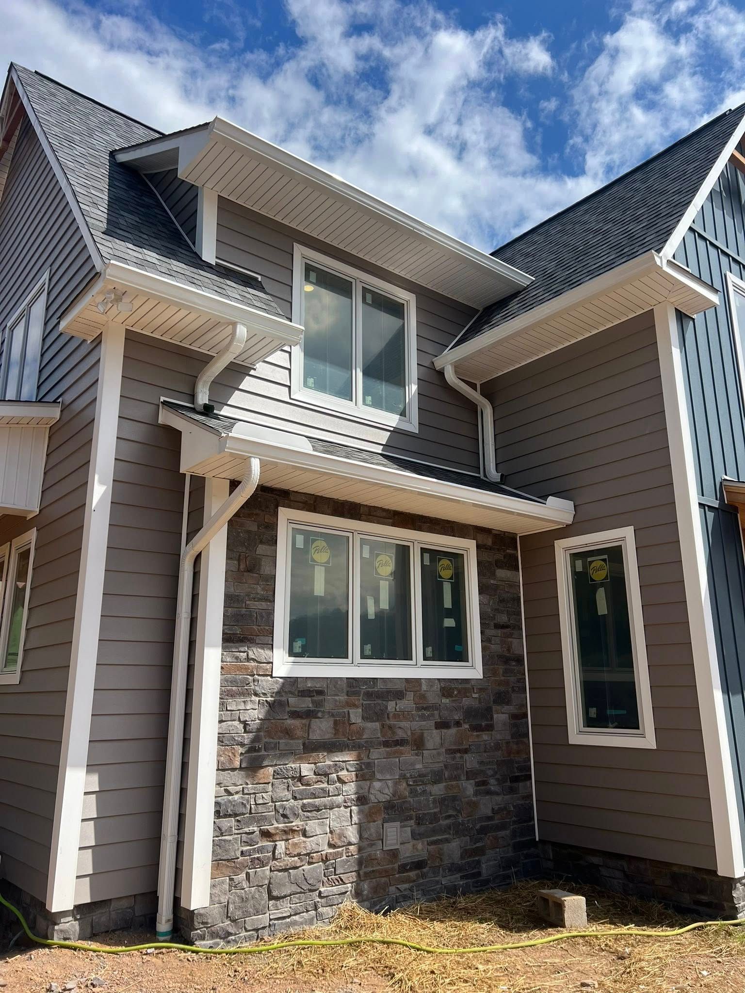 A modern two-story house exterior under construction, featuring gray horizontal siding, stone veneer, and white trim.
