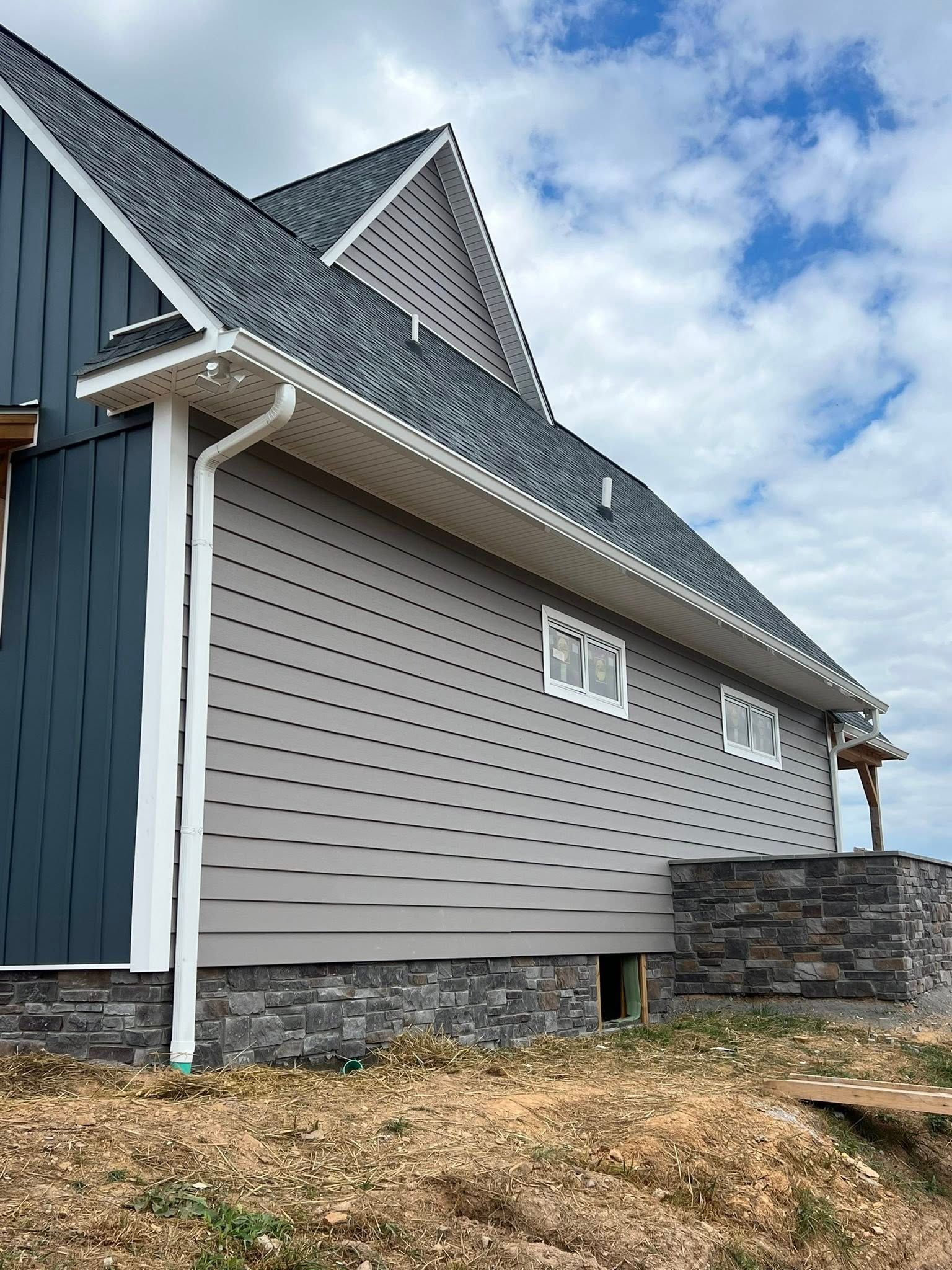 A side view of a house with navy blue vertical siding, light gray horizontal siding, and a stone foundation base.