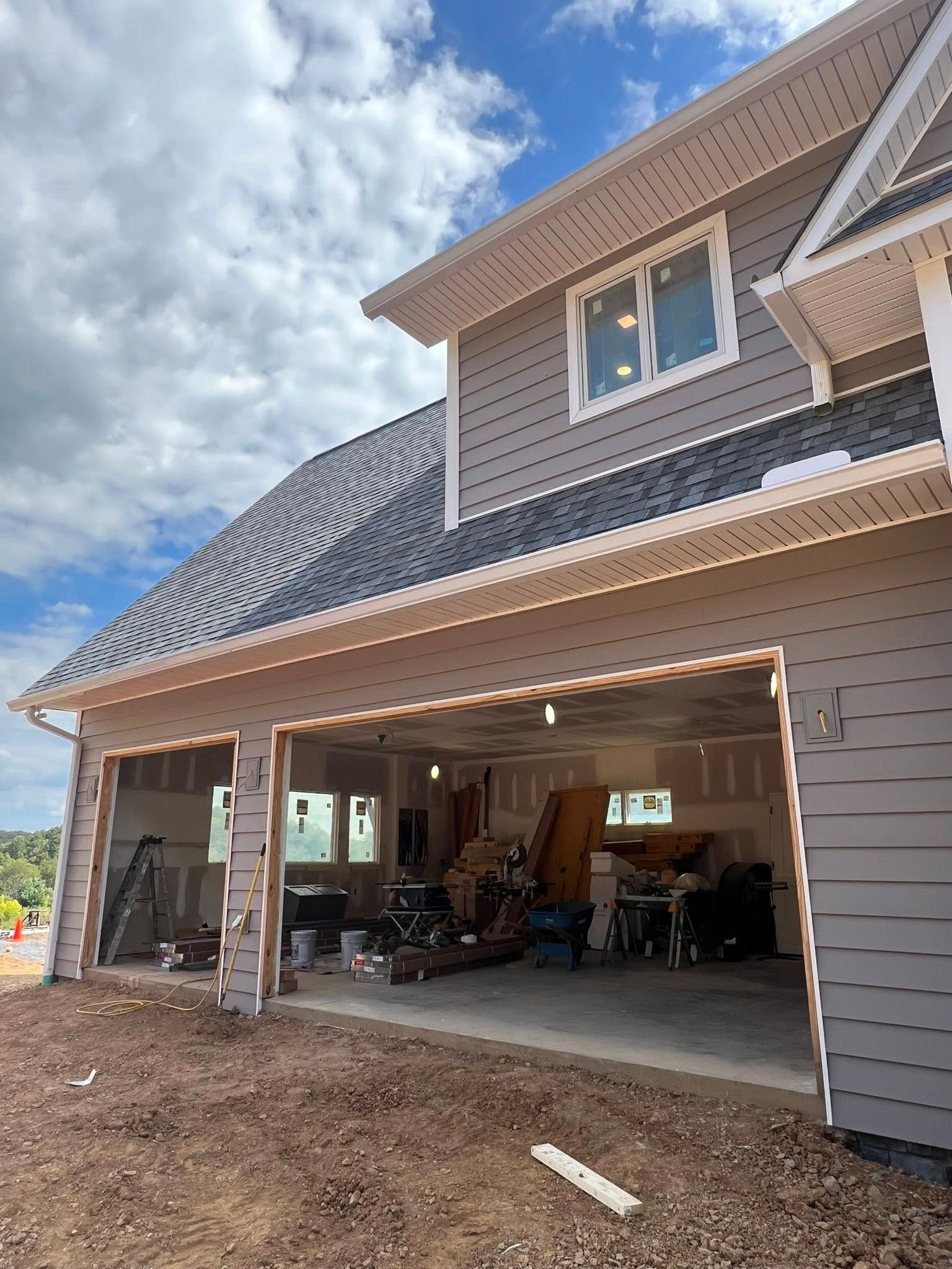 A newly constructed two-car garage with gray siding under a cloudy sky, with building materials visible inside.