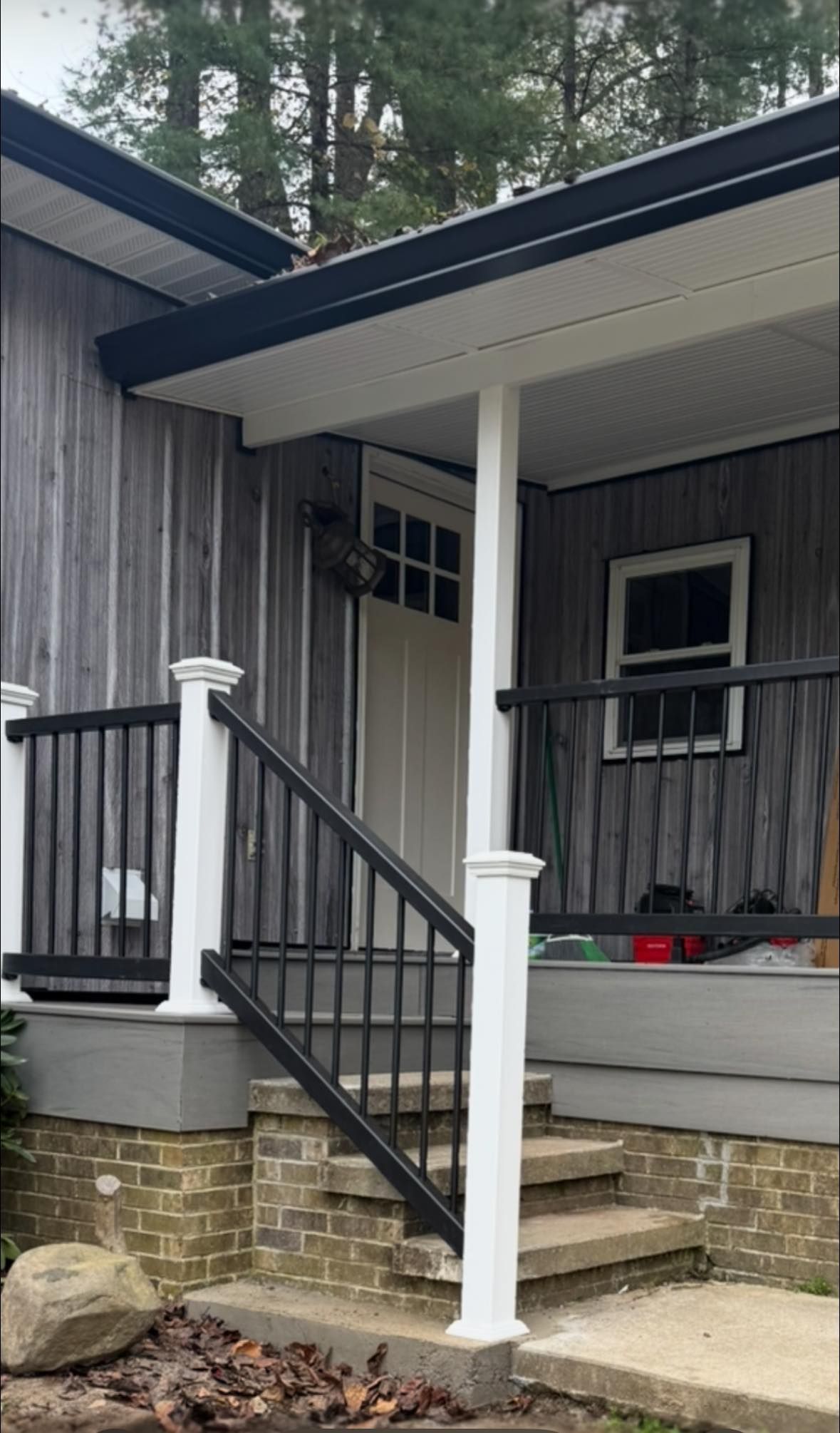 A front porch entrance with gray vertical siding, a white door, black railings, and stone foundation steps.