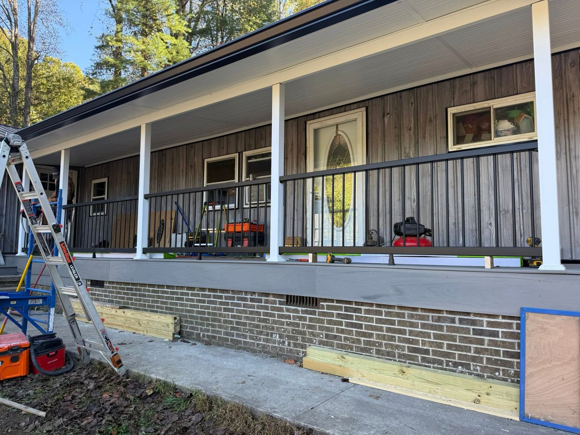 A wooden-sided house exterior with a porch, black railings, and a ladder leaning against the structure.