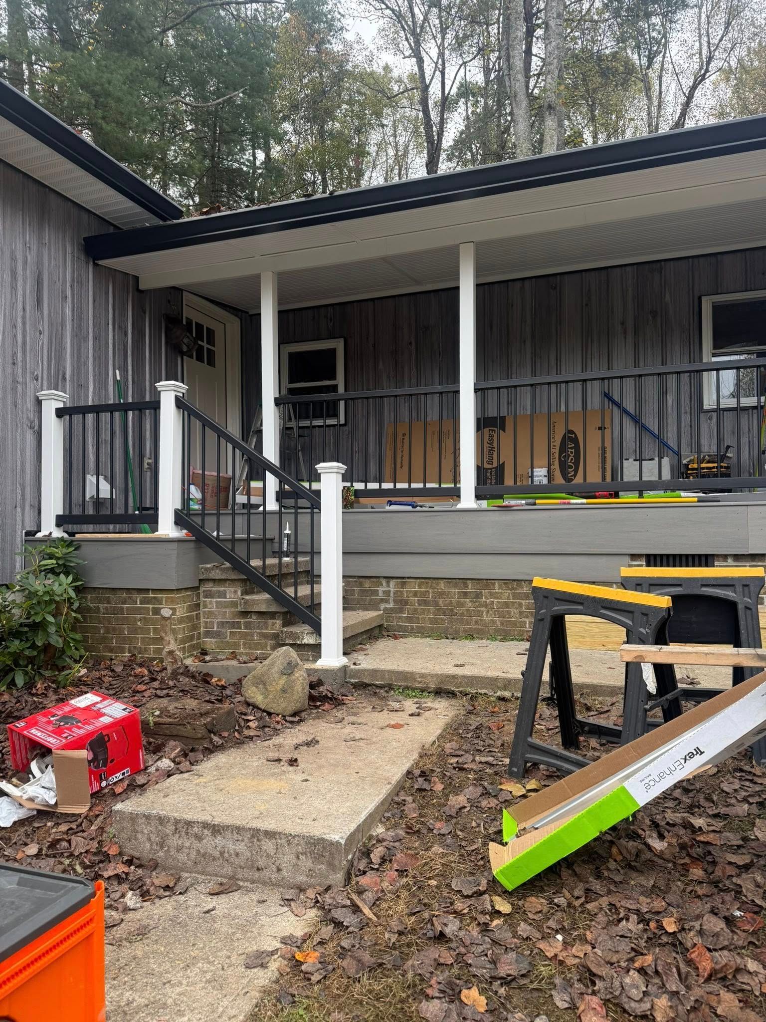 A gray house with a wooden deck under construction, featuring black railings, white posts, and building supplies outdoors.