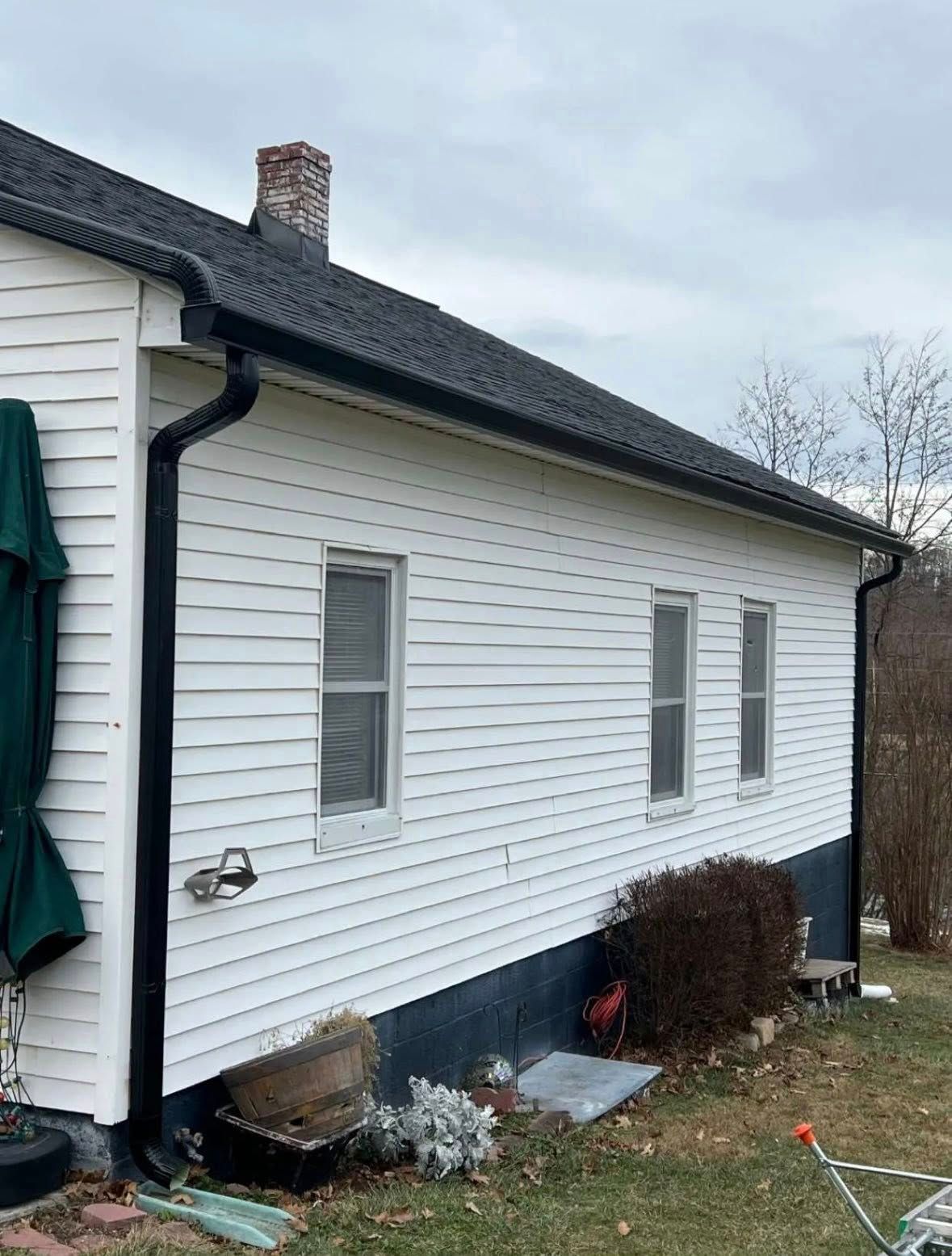A side view of a white, single-story house with a black roof, black gutters, and a dark-painted foundation.