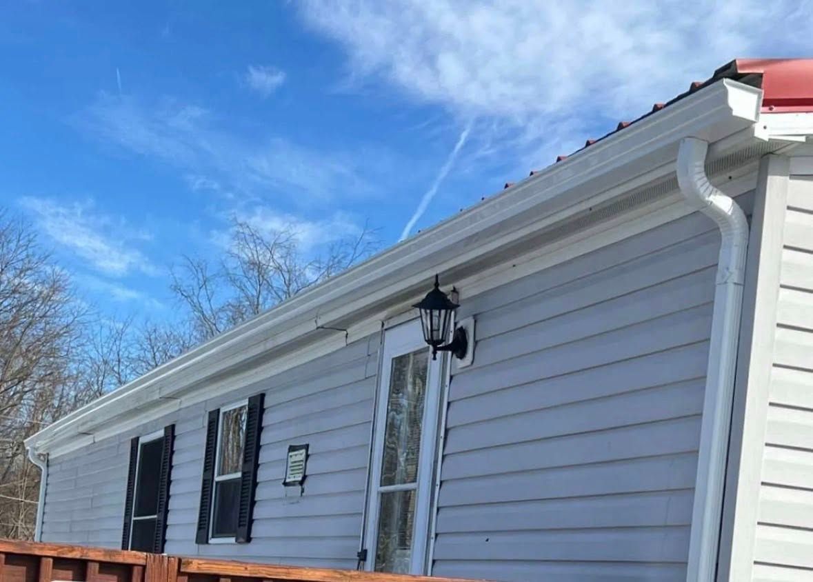 Low-angle view of a house exterior with light grey siding, white gutters, a black outdoor wall lamp, and a blue sky.