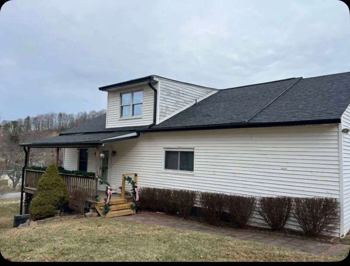 A one-story white house with a dark roof and a small wooden porch on a grassy lot under an overcast sky.