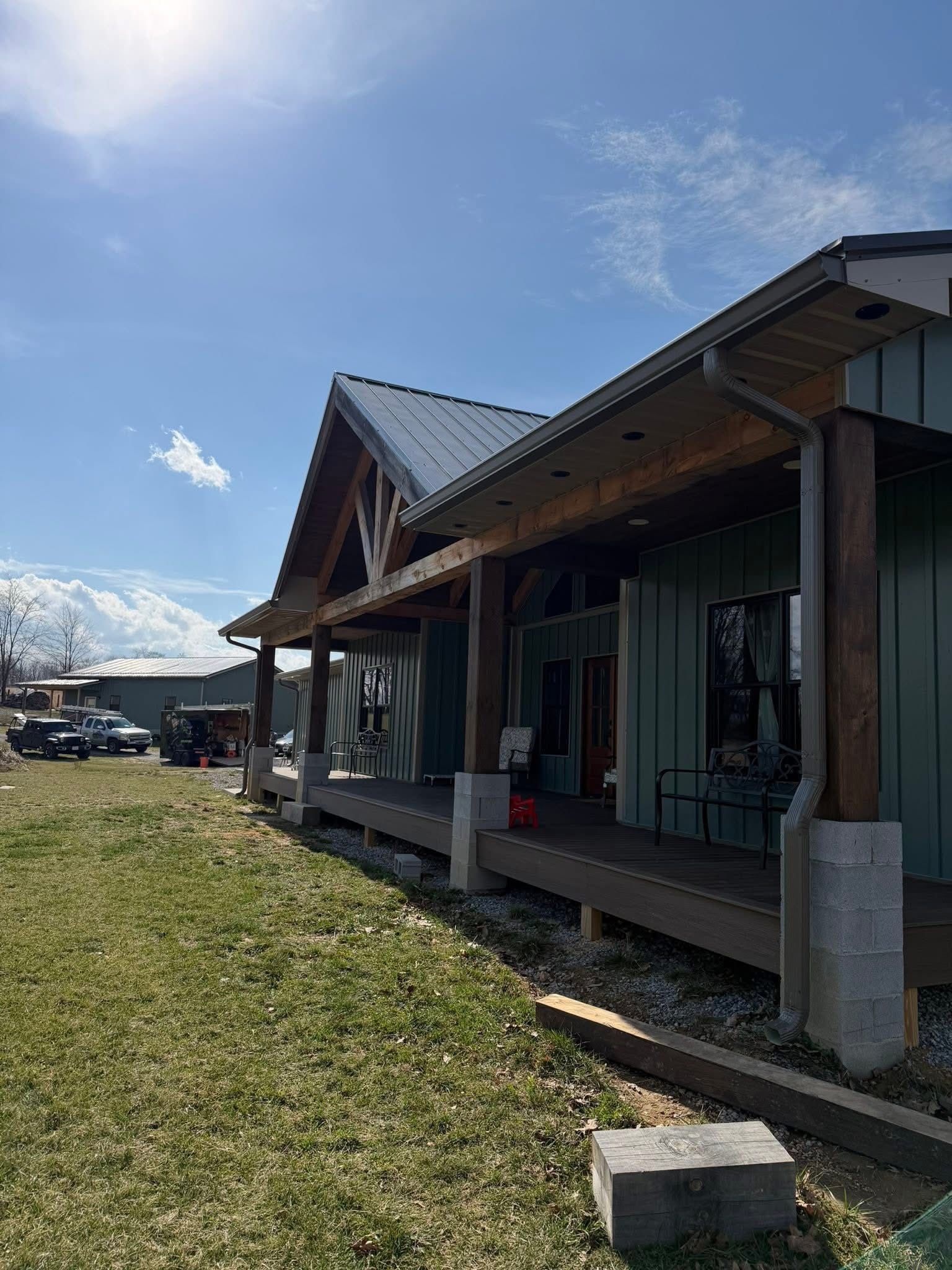 A sage green house with a covered wooden porch, metal roof, and exposed beam accents, seen from an angled perspective.