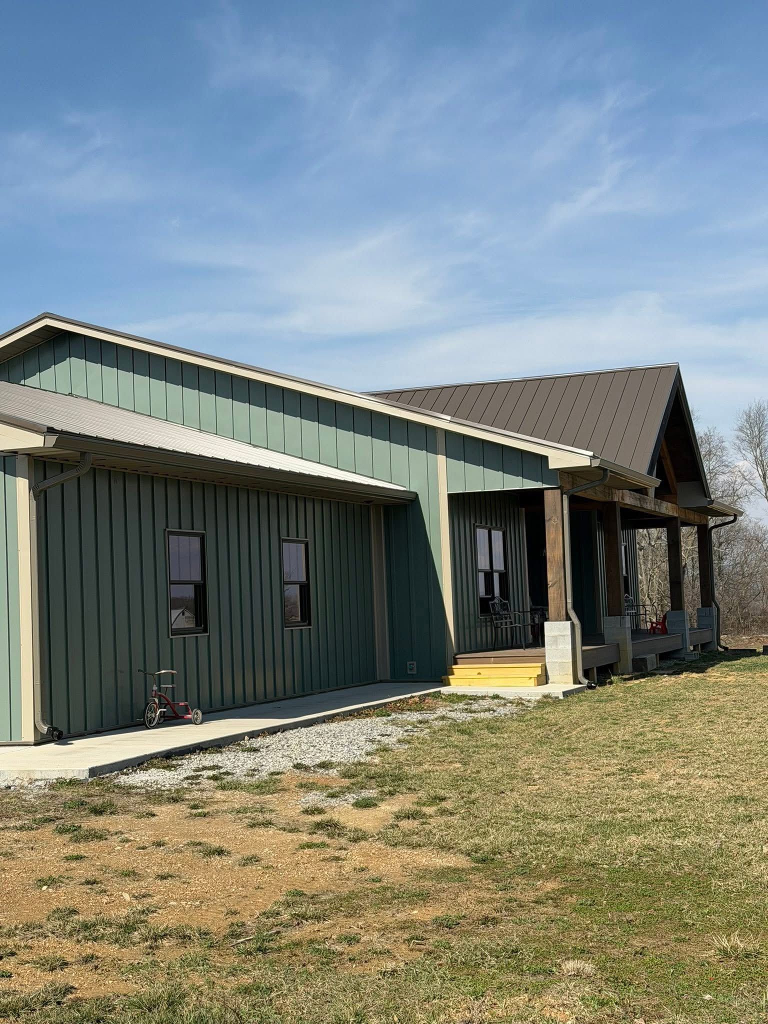 A sage green, modern farmhouse-style building with a metal roof and a covered porch on a sunny day.
