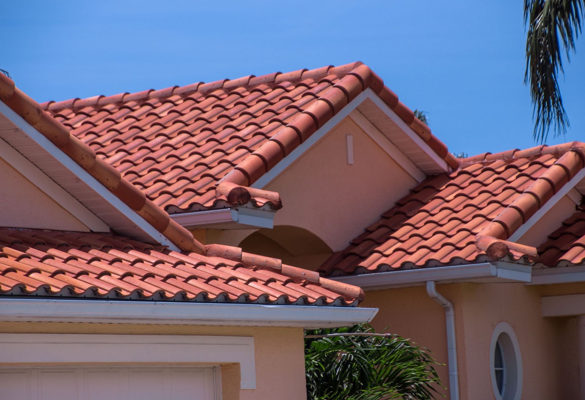 A close-up of a house with a terracotta-colored tile roof and pale orange exterior walls against a clear blue sky.