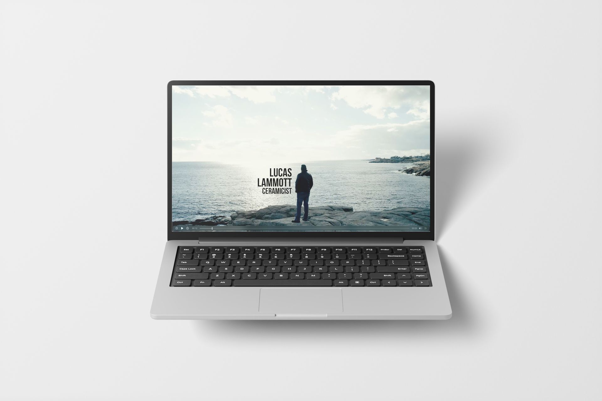Laptop showing a person standing on rocks by the ocean; text on screen: 