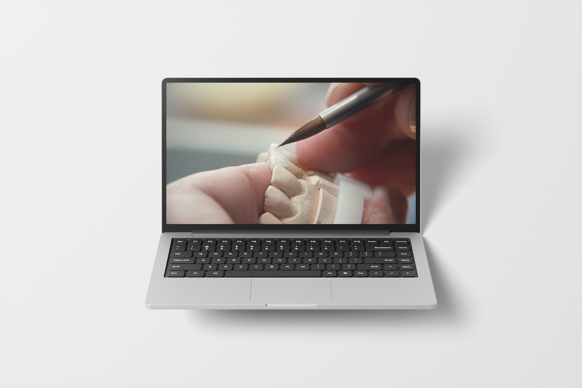Laptop displaying hand applying brush to dental model.